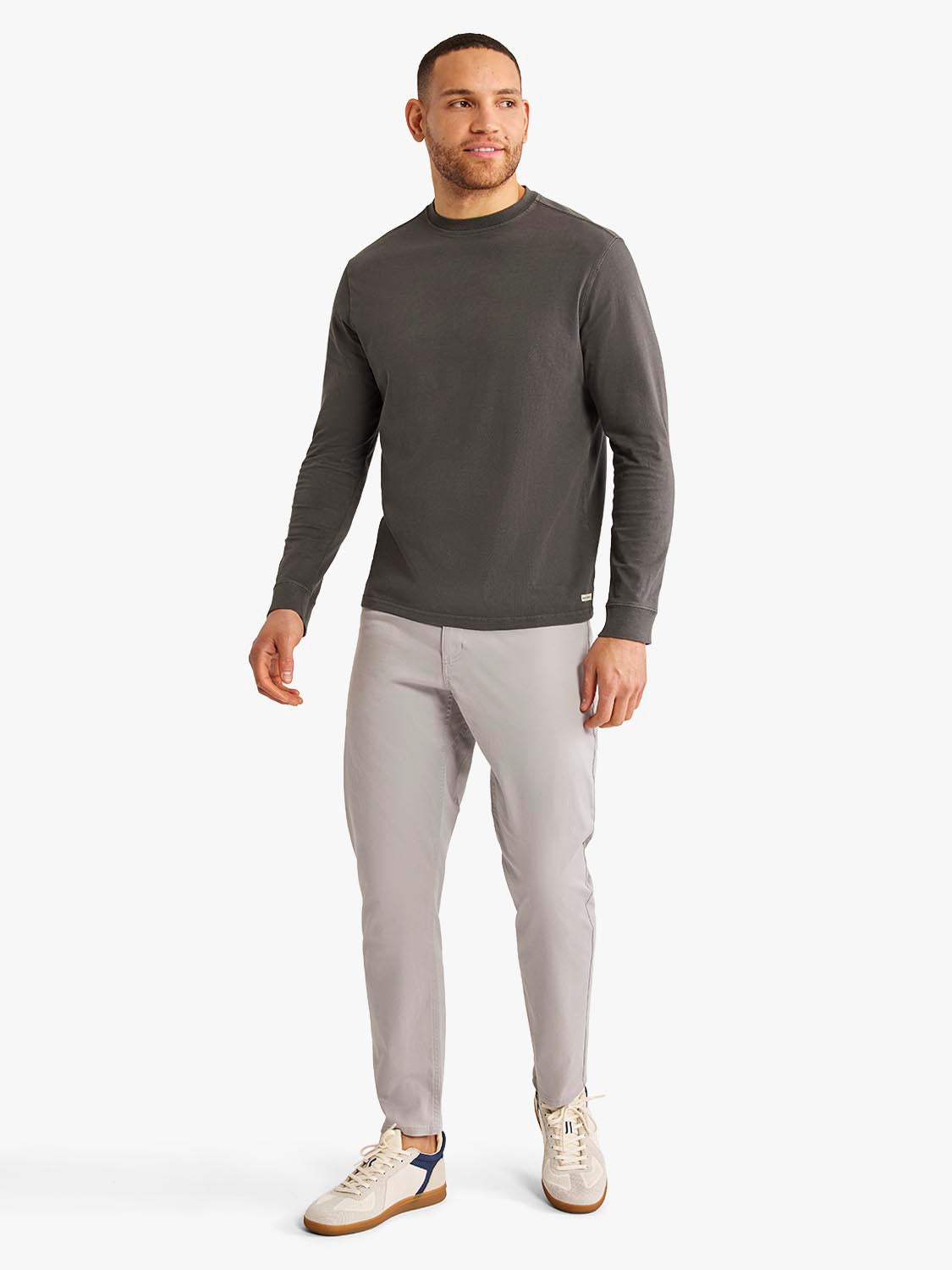 Man wearing a black long sleeve crew neck tee with light gray pants and cream sneakers.