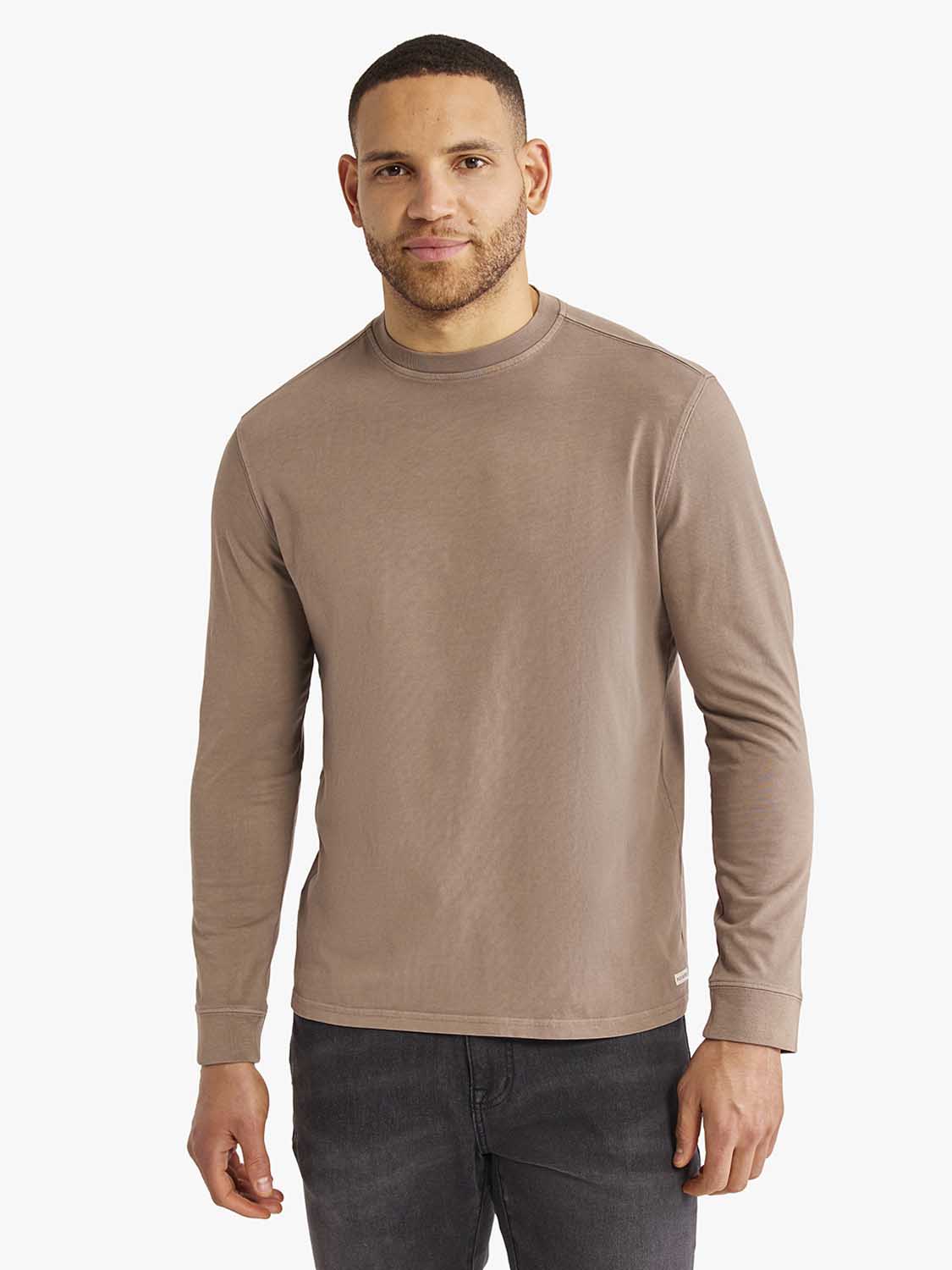 Man wearing a sandbar-colored long sleeve tee with a crew neckline and dark jeans.