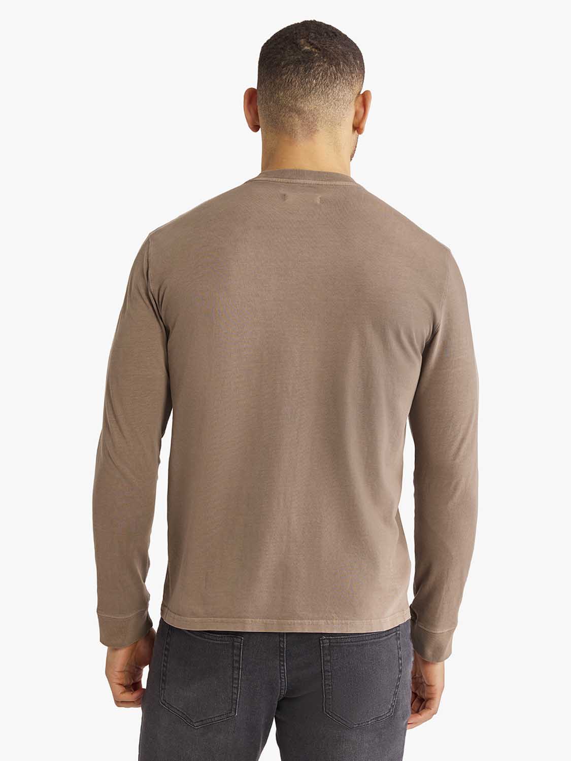 Man wearing a taupe long sleeve tee with dark gray jeans, shown from the back.