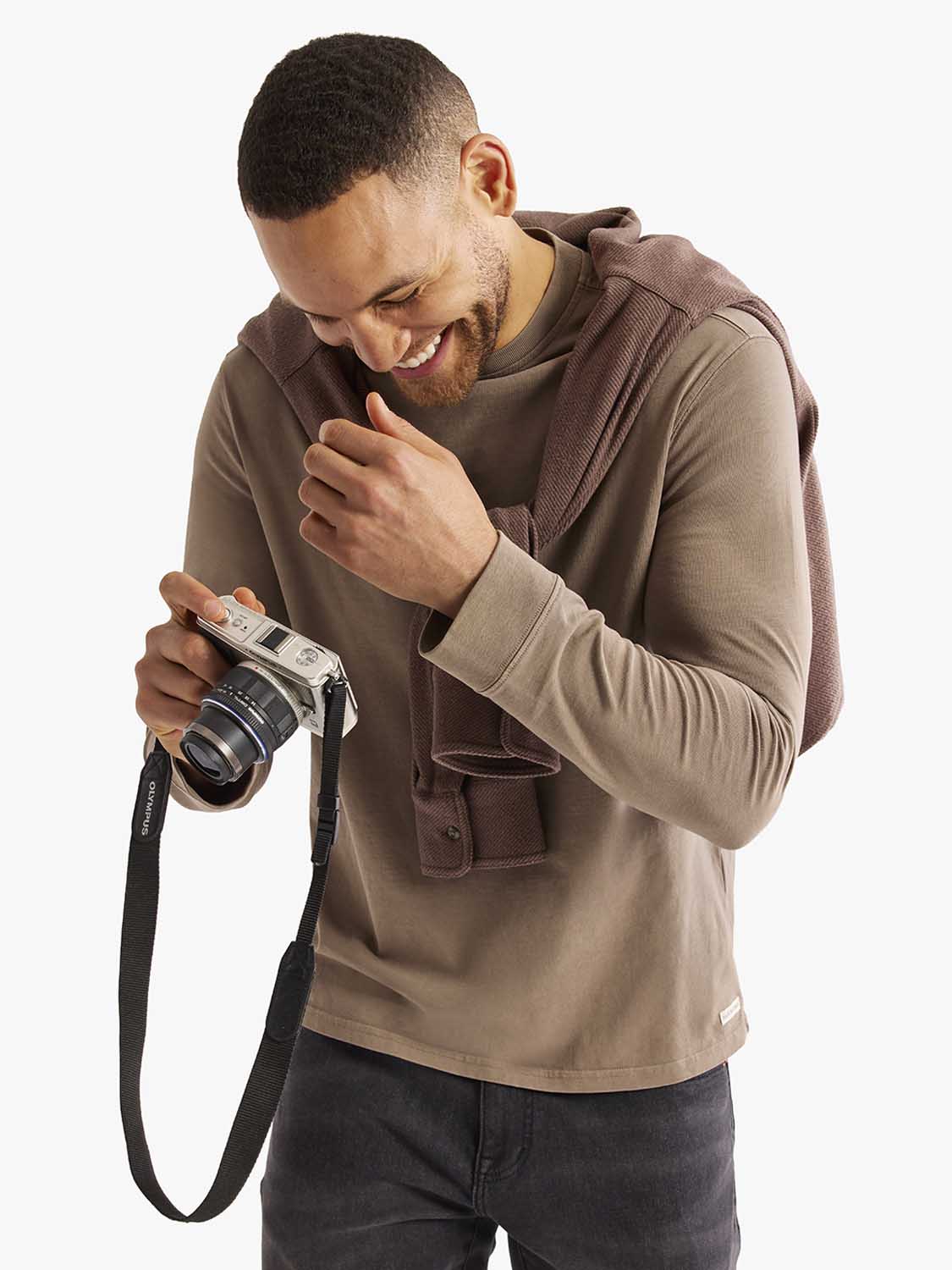 Man wearing a brown long sleeve tee layered under a textured cardigan while holding a vintage camera.