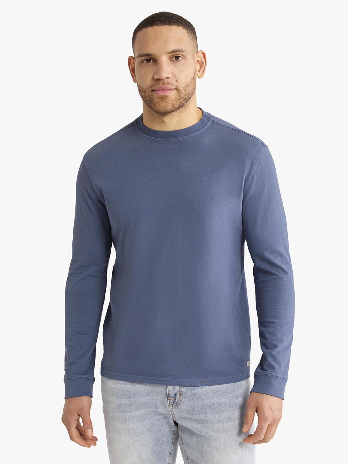 Man wearing a navy long sleeve crew neck tee with light blue jeans against a white background.