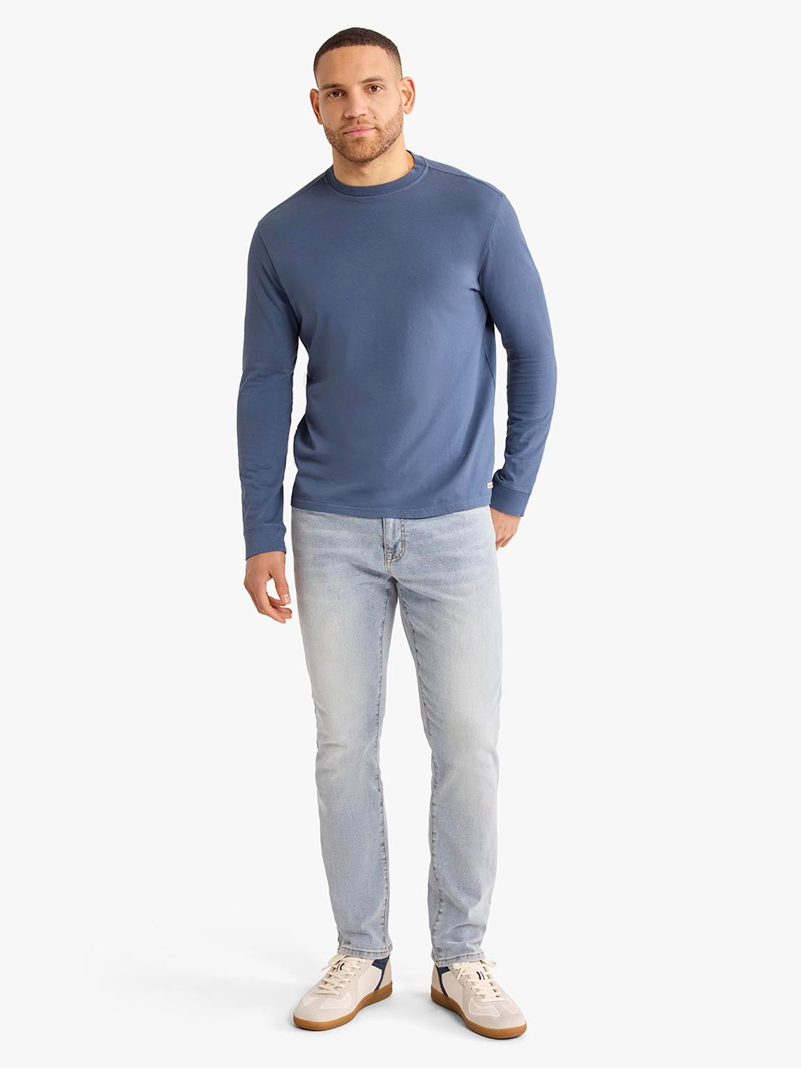 Man wearing a navy long sleeve crew neck tee with light wash jeans and cream sneakers.