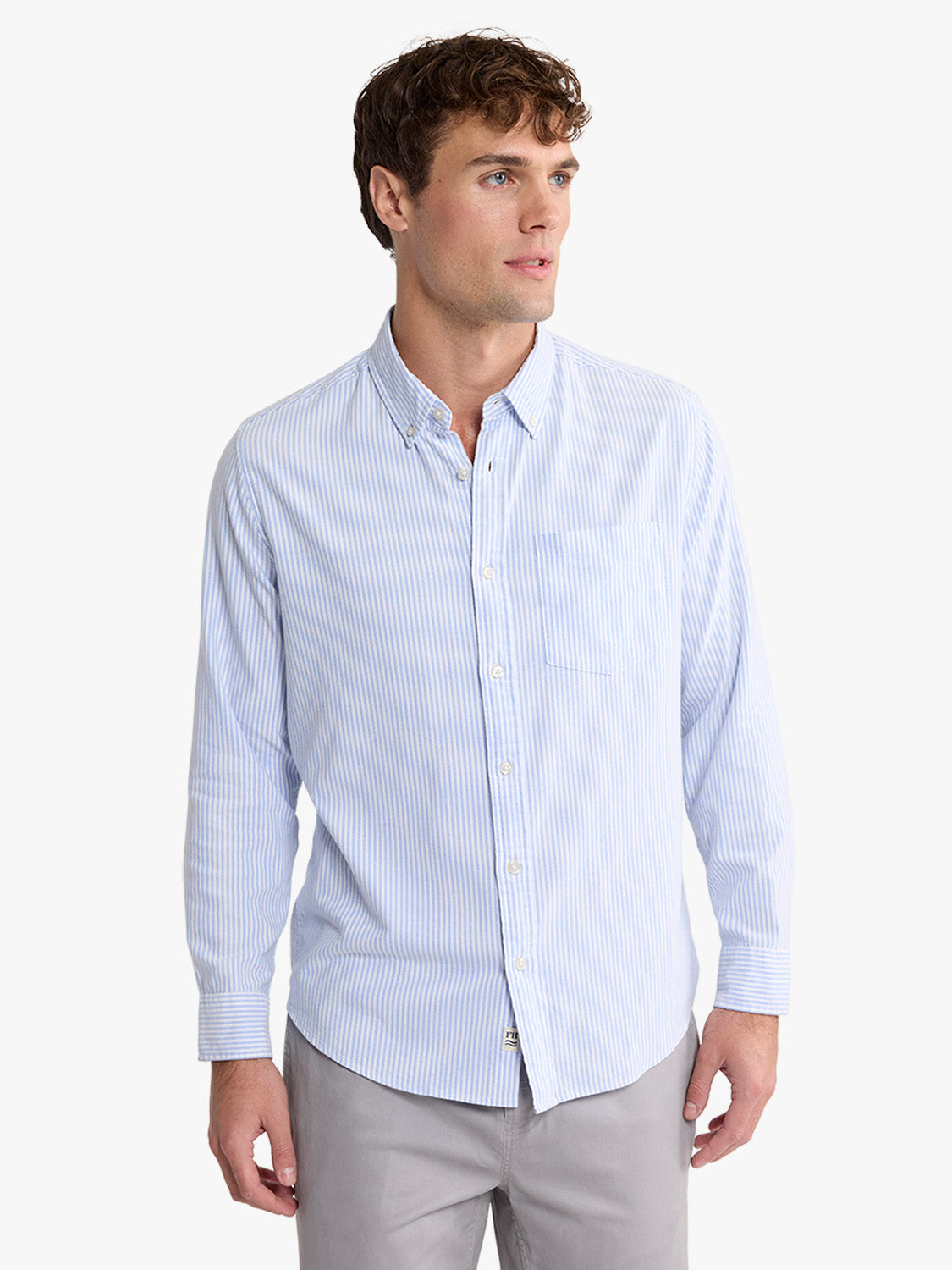 Man wearing a light blue striped oxford shirt with long sleeves and button-front closure.