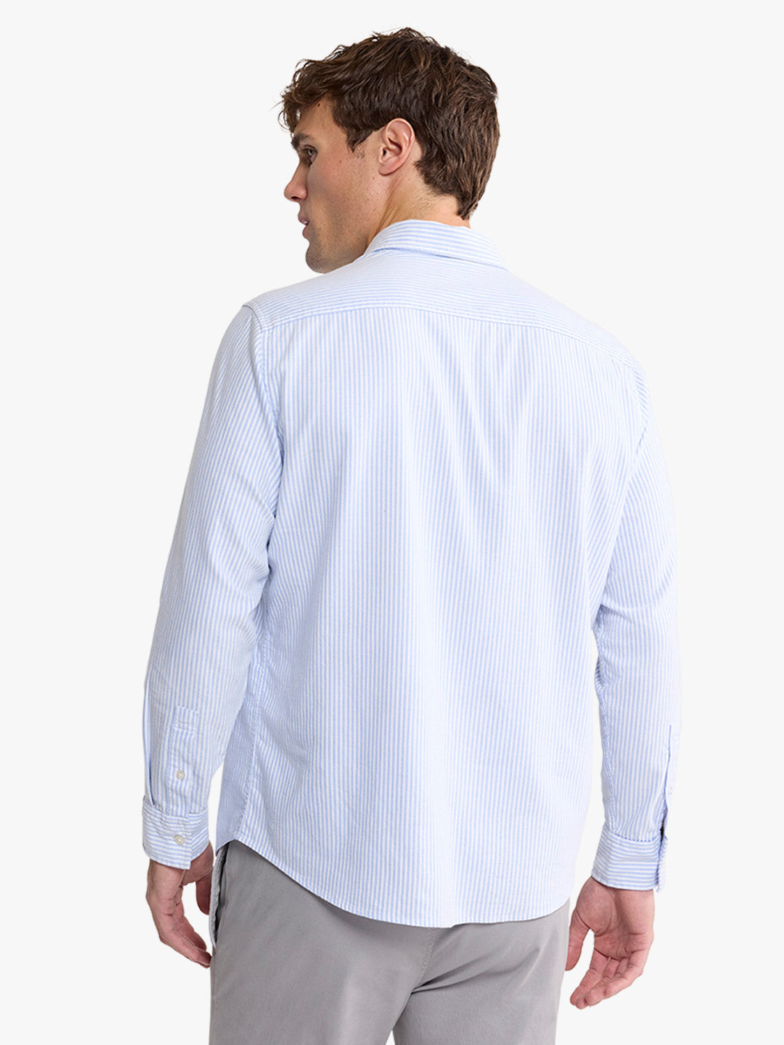 Man wearing a light blue striped oxford shirt with long sleeves and a collar, shown from behind.