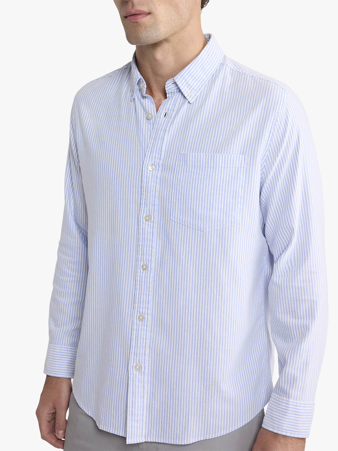 Man wearing a light blue and white striped oxford shirt with long sleeves and button front closure.