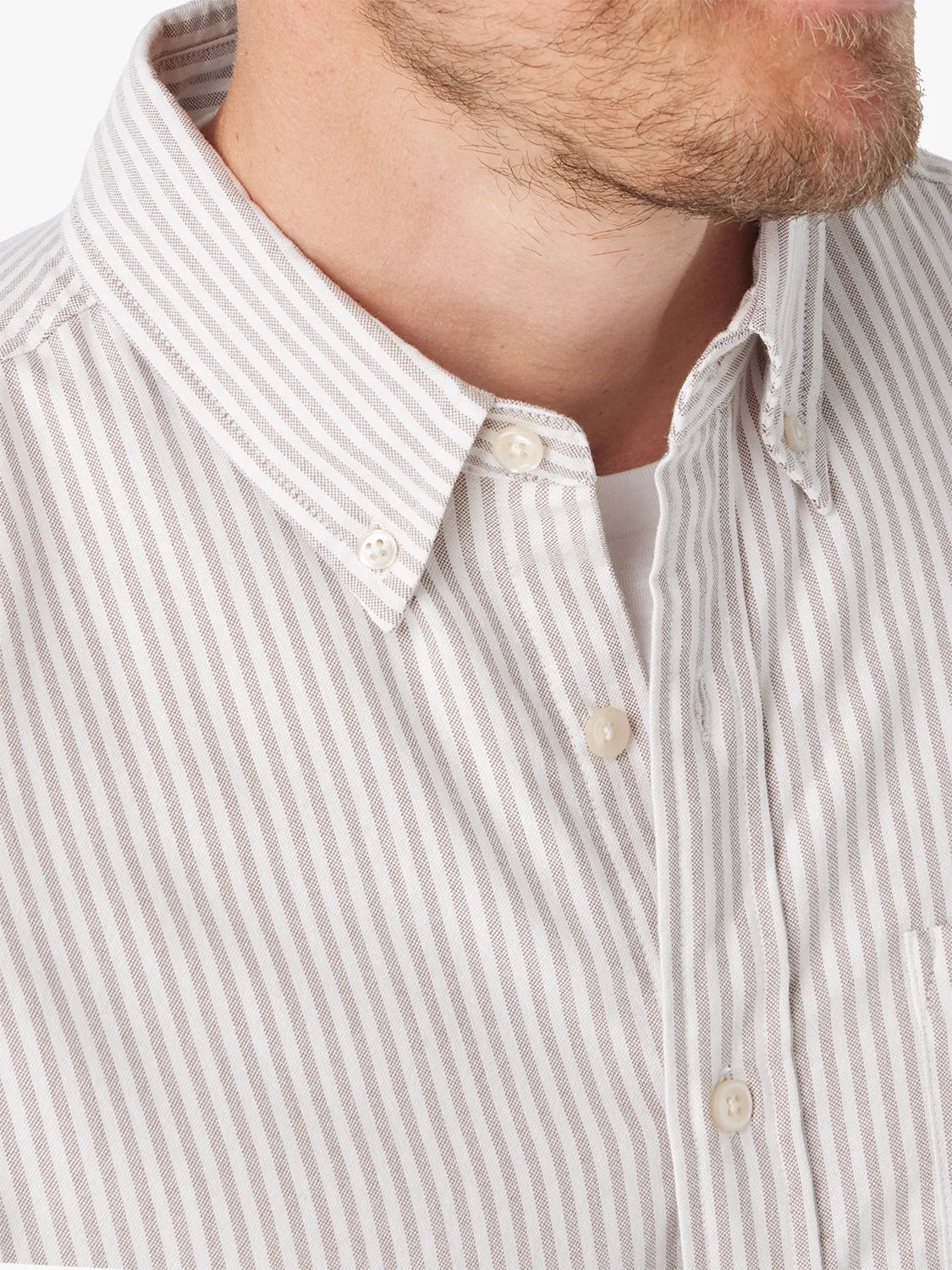 Man wearing a light tan and white striped Oxford shirt with white button closure and collar detail.