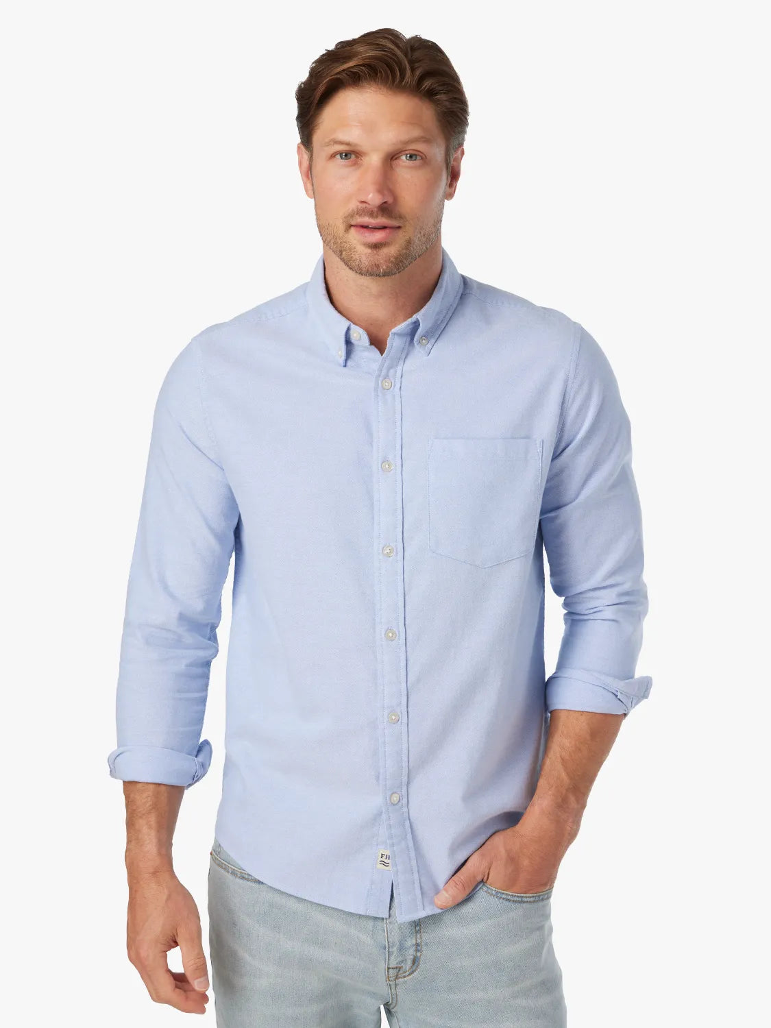 Man wearing a light blue button-down oxford shirt with rolled sleeves and a chest pocket.