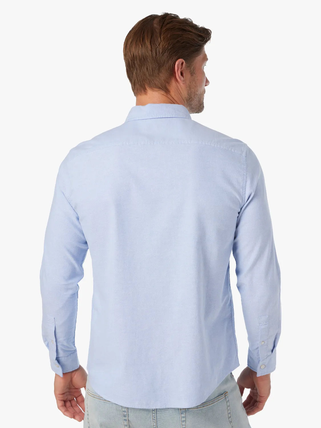 Man wearing a light blue long-sleeve oxford shirt, shown from the back view.