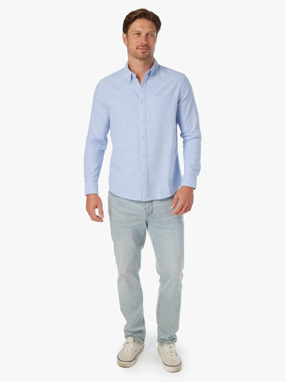 Man wearing a light blue button-down oxford shirt with long sleeves and light-wash jeans.