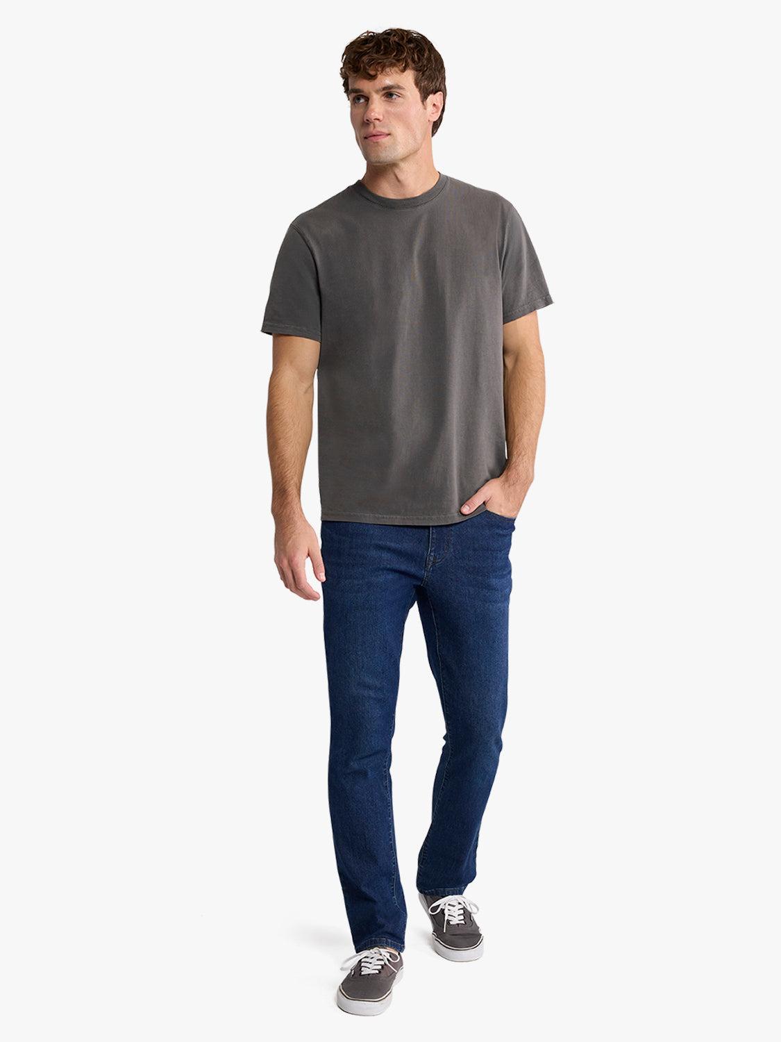 Man wearing a charcoal gray short-sleeve crew neck t-shirt with dark blue jeans and gray sneakers.