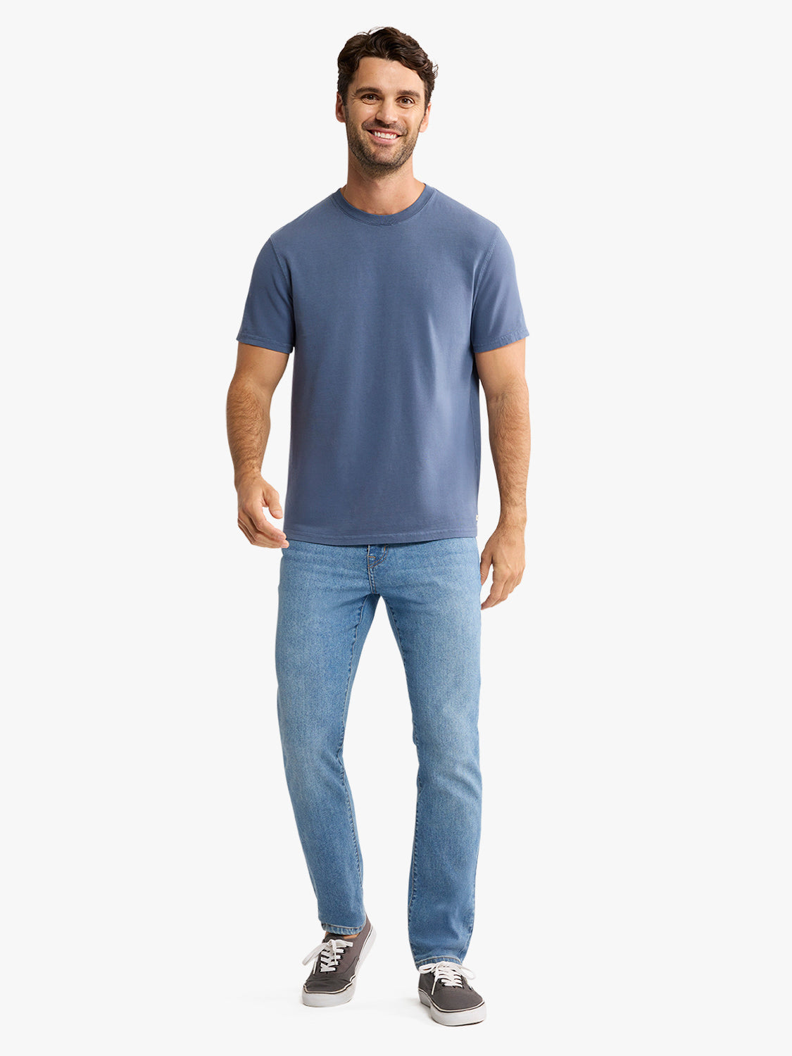 Man wearing a navy blue short-sleeved crewneck tee with light blue jeans and dark sneakers.