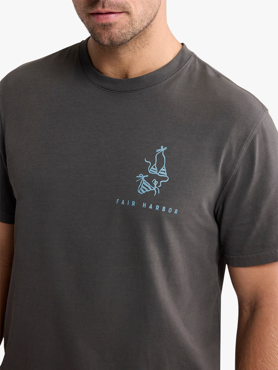 Man wearing a charcoal gray t-shirt with a small blue sailboat graphic and 