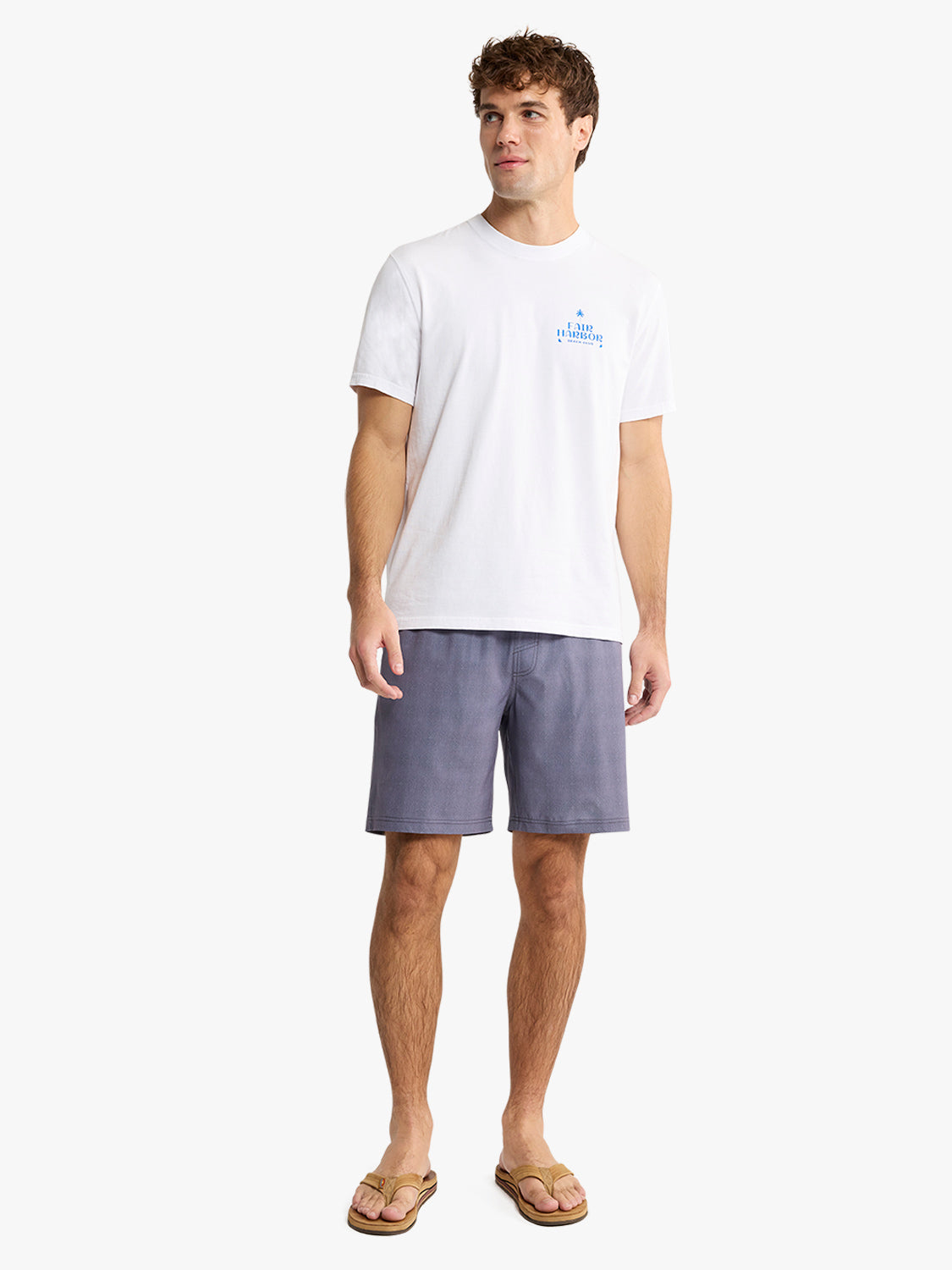Man wearing white graphic tee with blue chest logo and gray shorts with sandals.