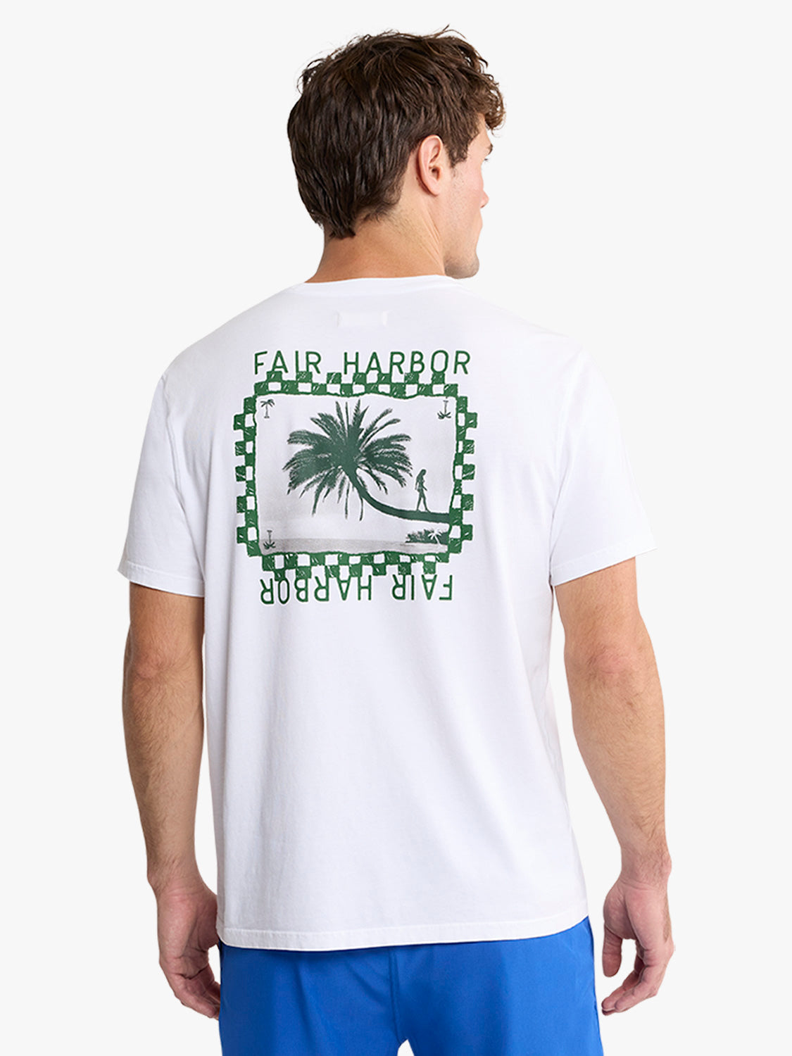 Man wearing white t-shirt with green checkered border and palm tree graphic on back.