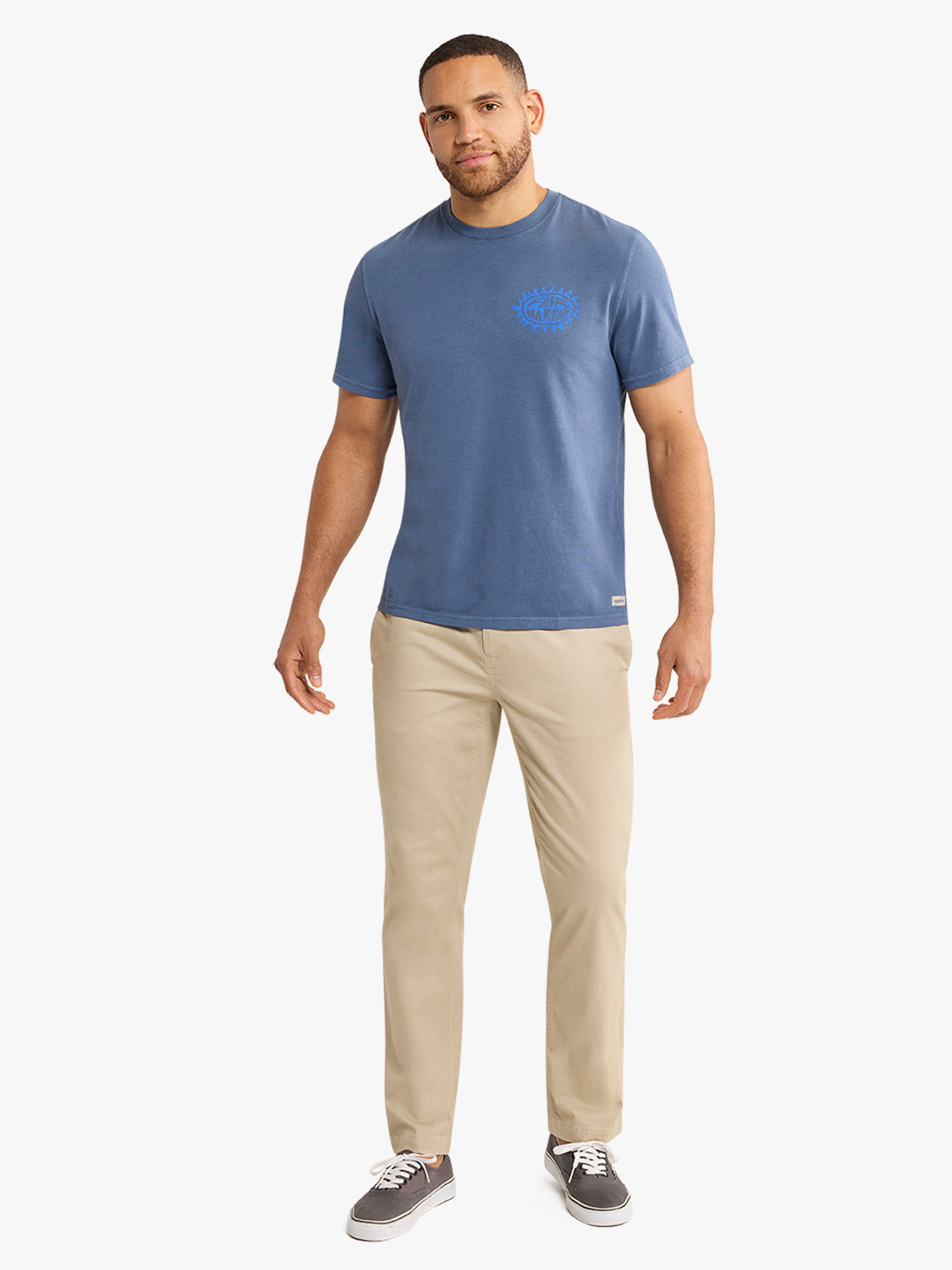 Man wearing a blue-gray graphic t-shirt with small chest logo and beige pants.