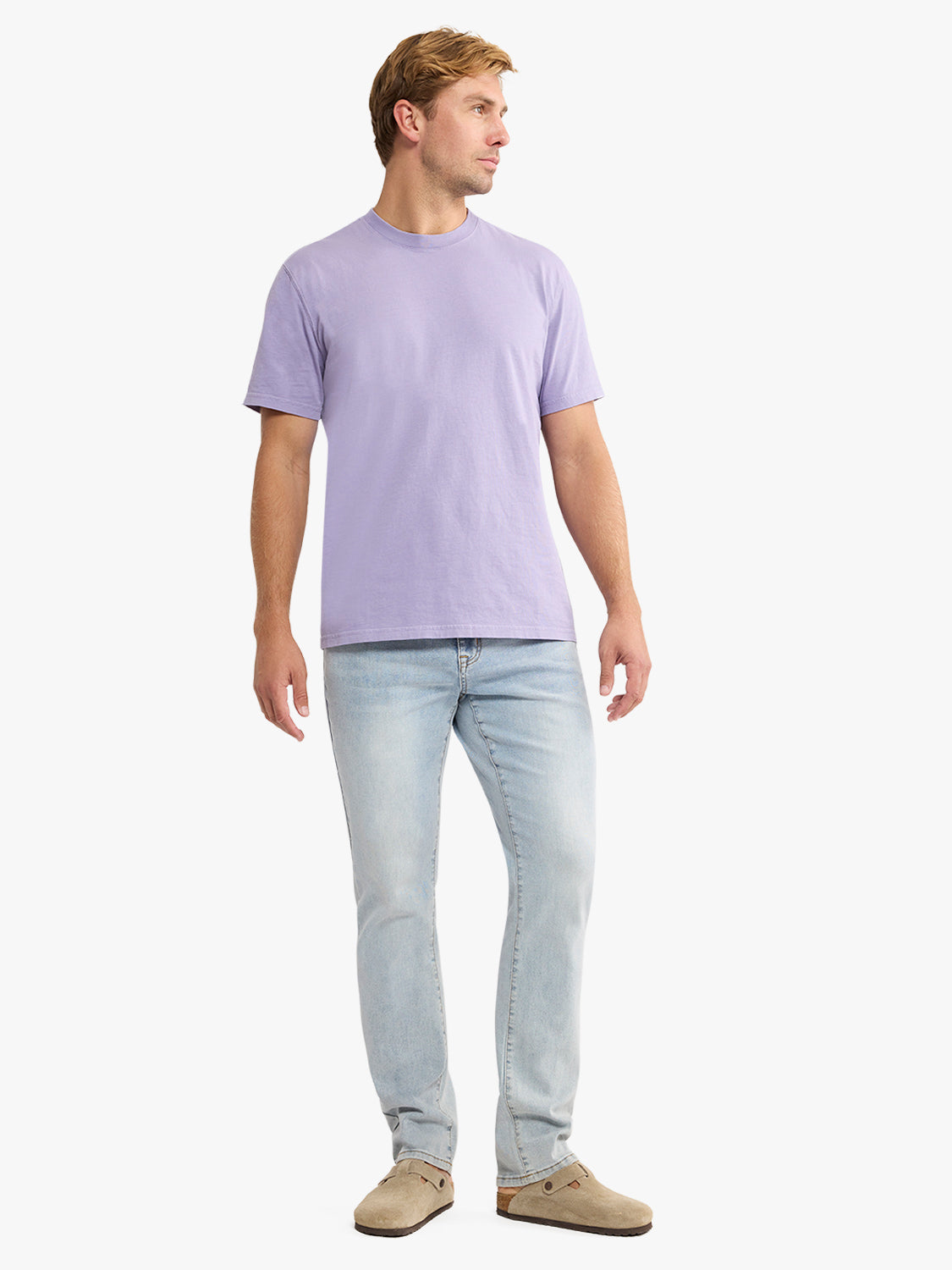 Man wearing a light purple short-sleeve crew neck tee shirt with light wash jeans and tan suede shoes.