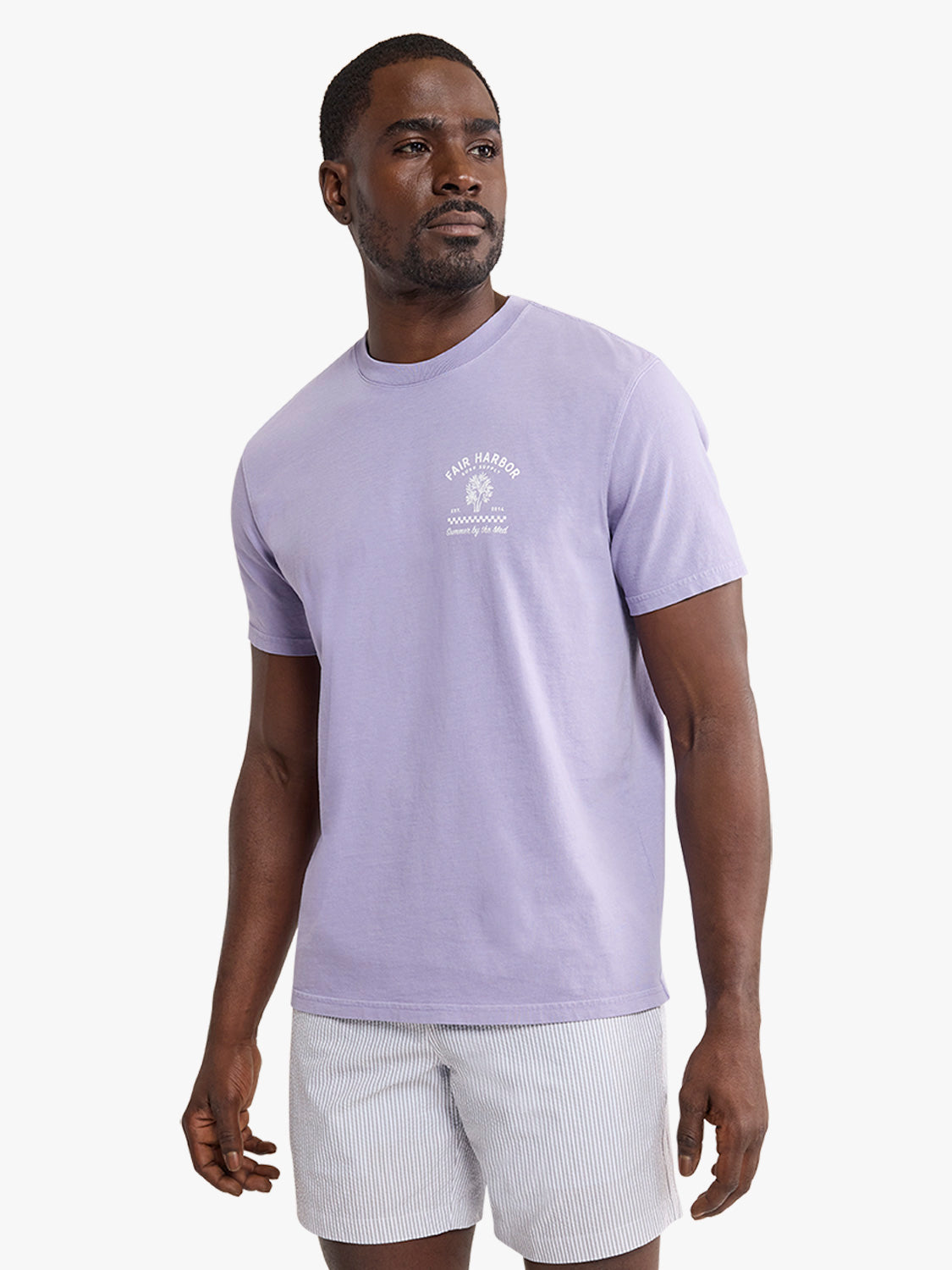 Man wearing lavender short-sleeve graphic tee with small chest print and striped shorts.