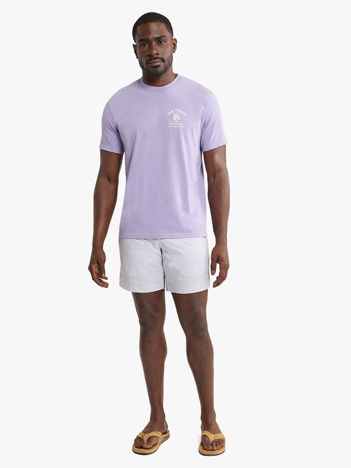 Man wearing a lavender graphic tee with small chest graphic and light striped shorts.