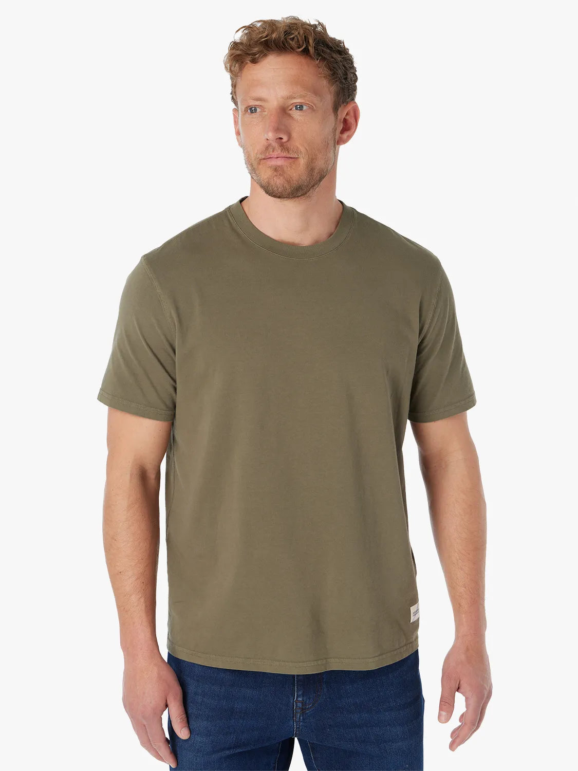 Man wearing olive green saltaire t-shirt on a white background paired with a pair of driftwood denim. 