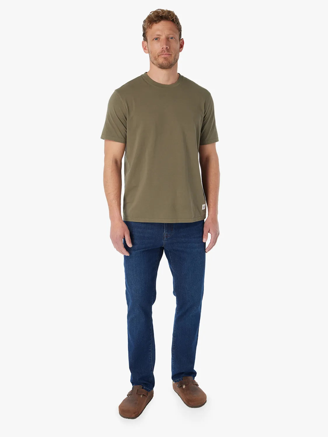 Man wearing olive green saltaire t-shirt on a white background paired with a pair of driftwood denim. 