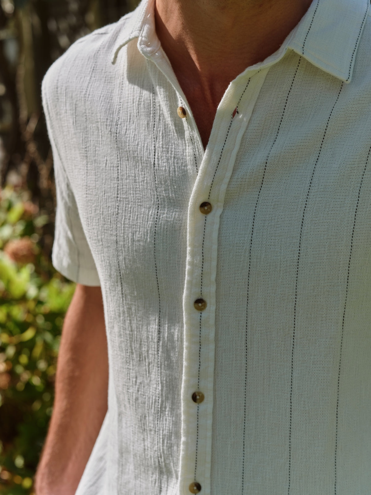 Man wearing a cream-colored textured short-sleeve shirt with vertical stripe pattern and button front.