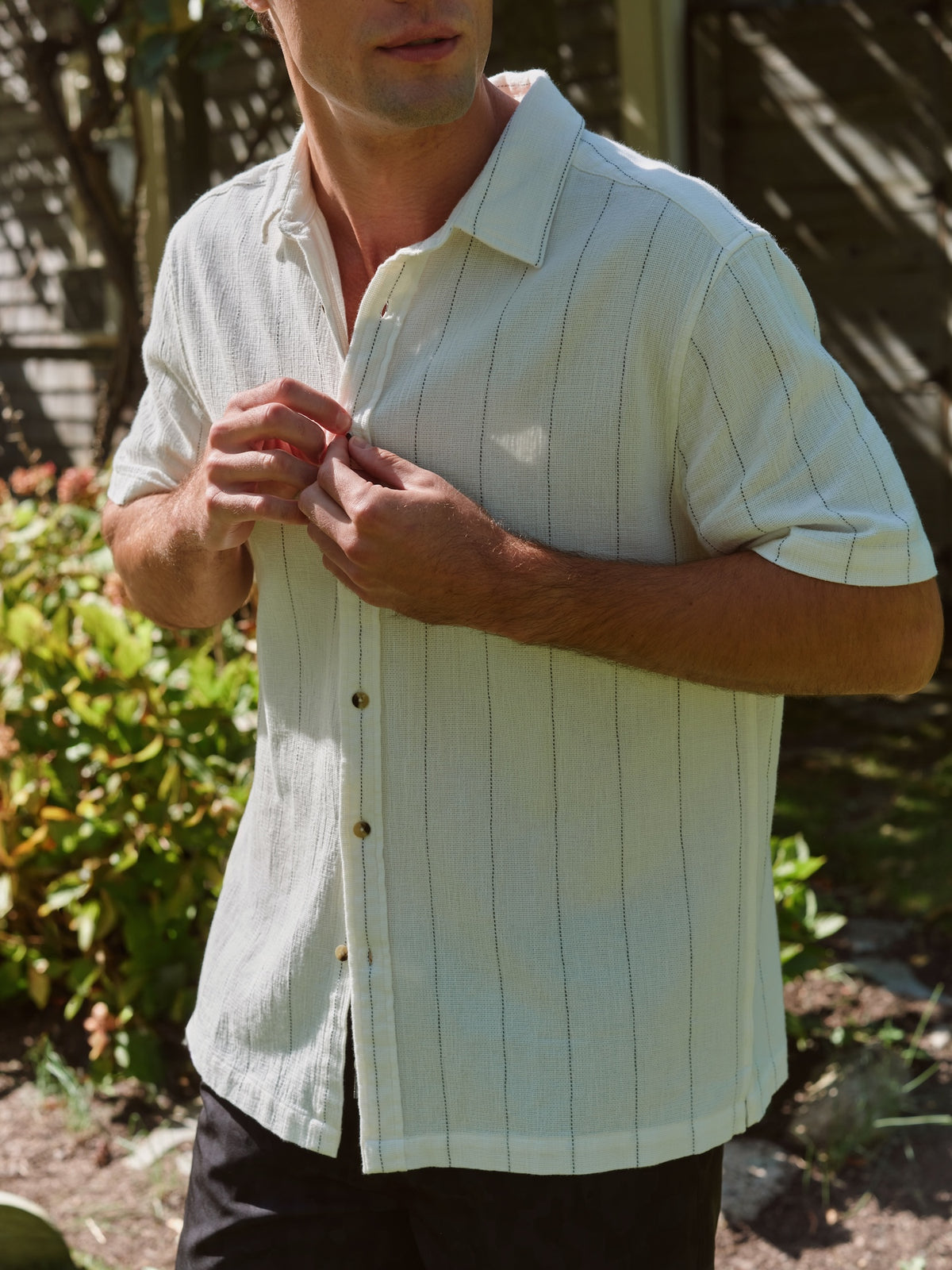 Man wearing a light green striped short-sleeve shirt with a textured fabric finish outdoors.