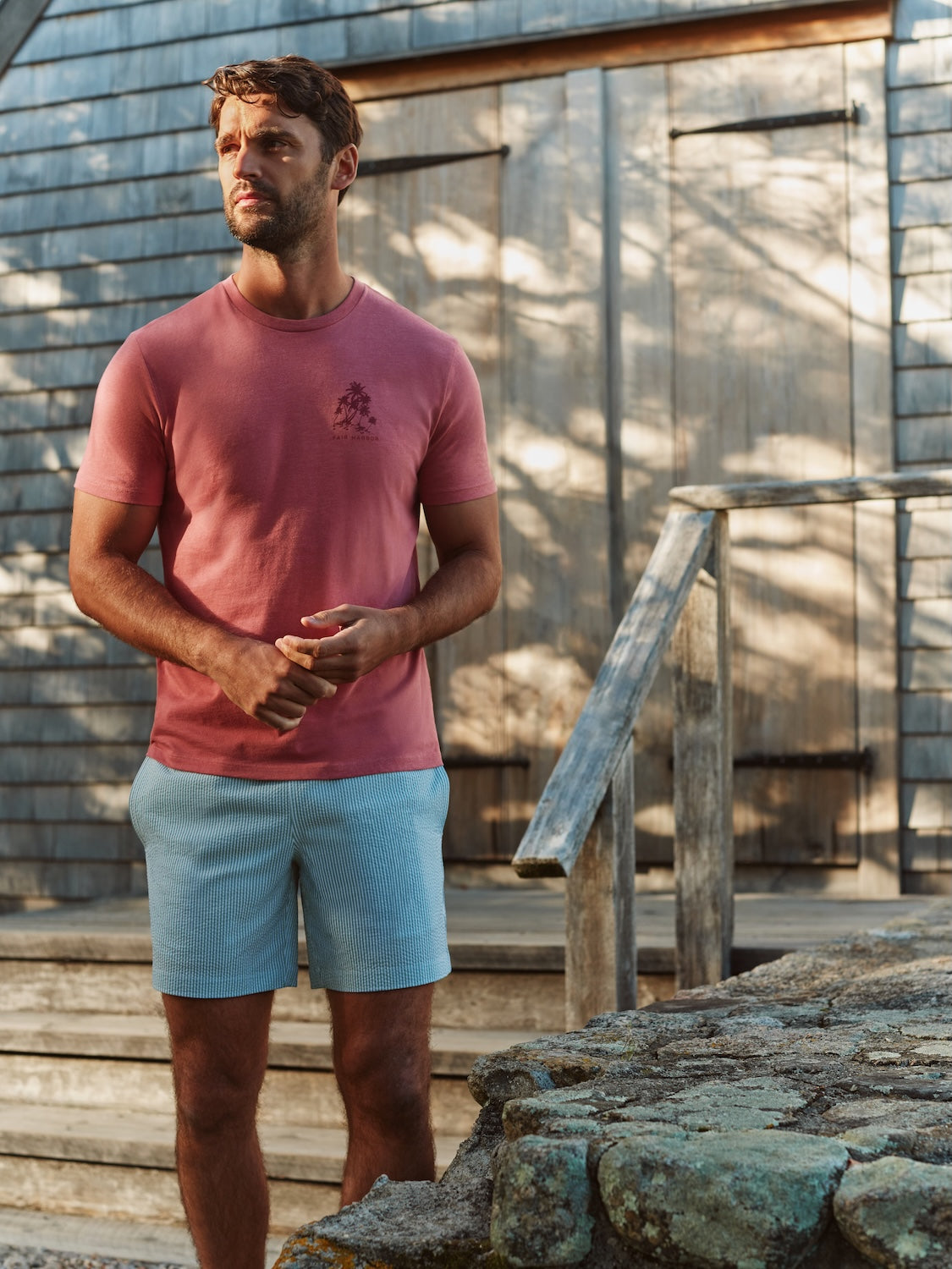 Man wearing a red short-sleeve t-shirt with small chest graphic and light blue shorts outdoors.