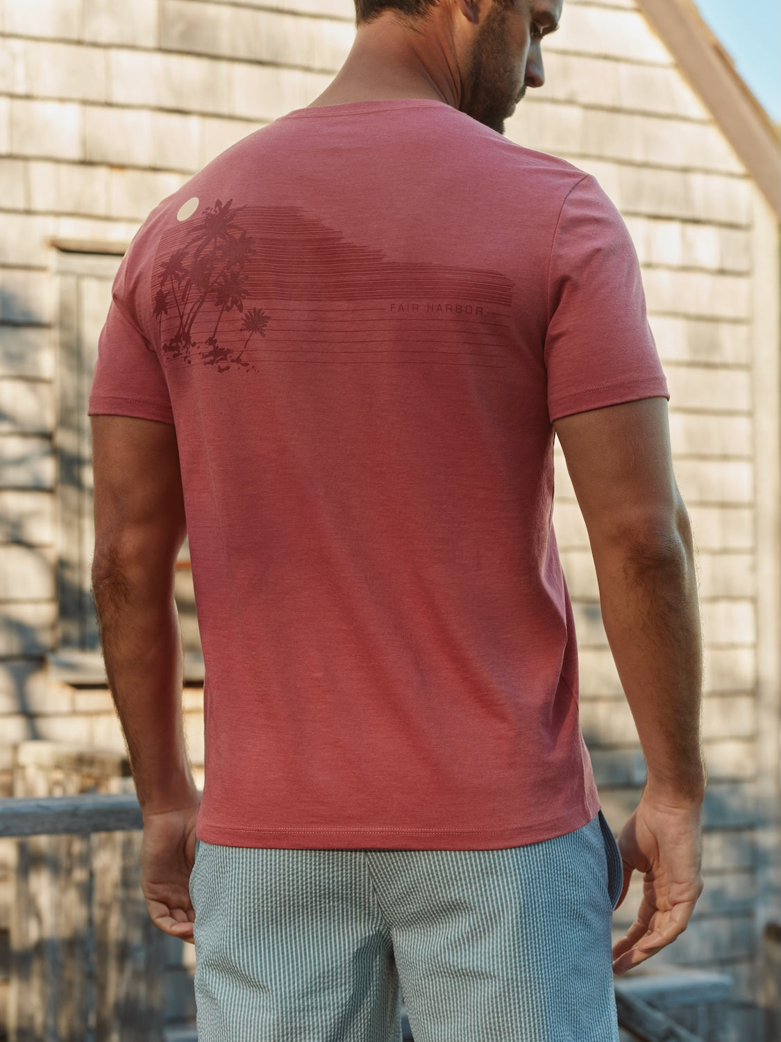 Man wearing a red short-sleeved t-shirt with palm tree graphic and text on back.