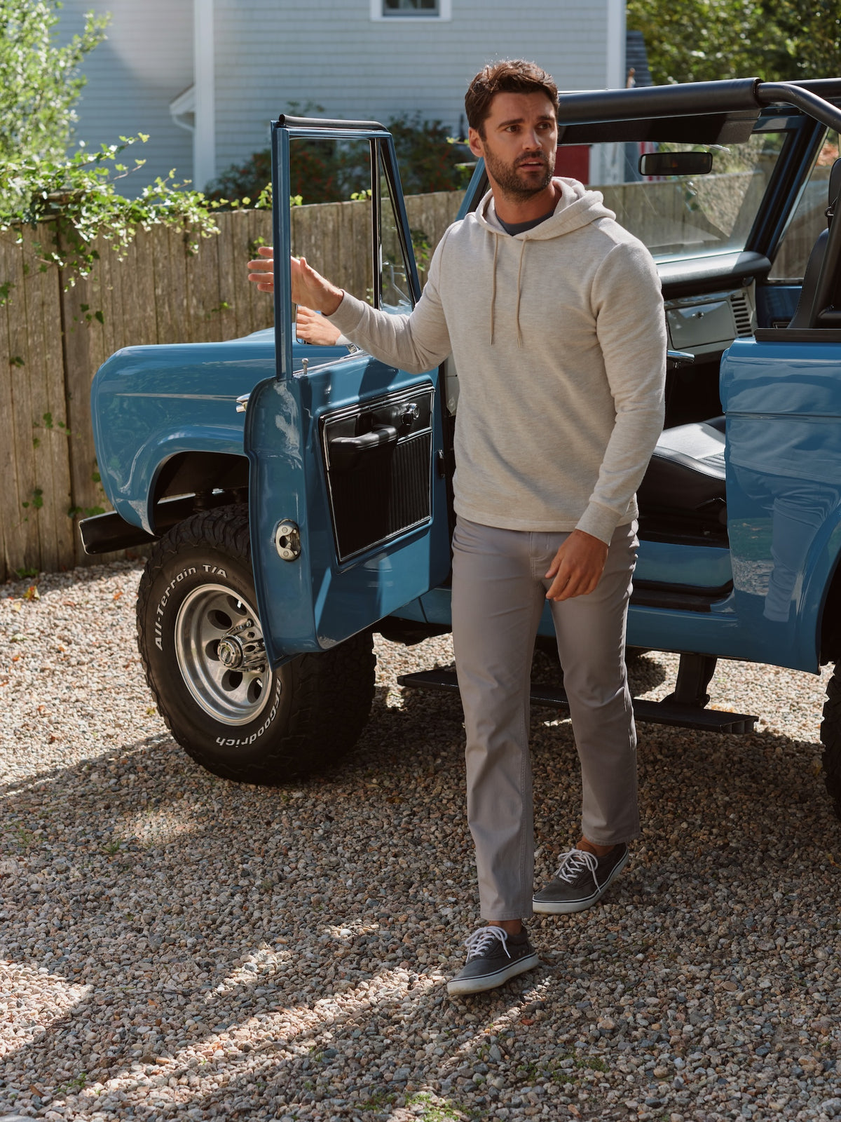 Man wearing a light blue hoodie and gray pants standing beside a blue vintage truck.