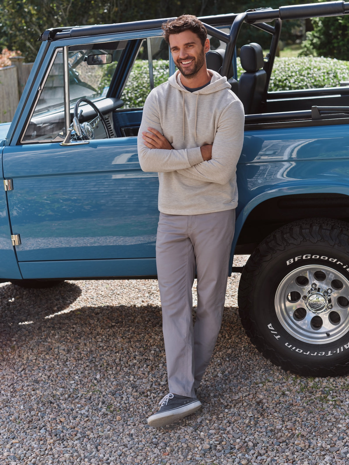 Man wearing a natural-colored hoodie standing beside a blue vintage truck.