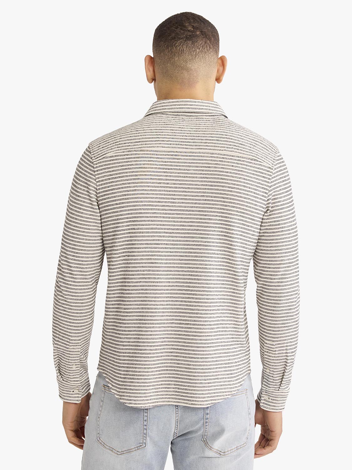 Man wearing a beige and white striped long-sleeve button-up shirt, shown from behind.