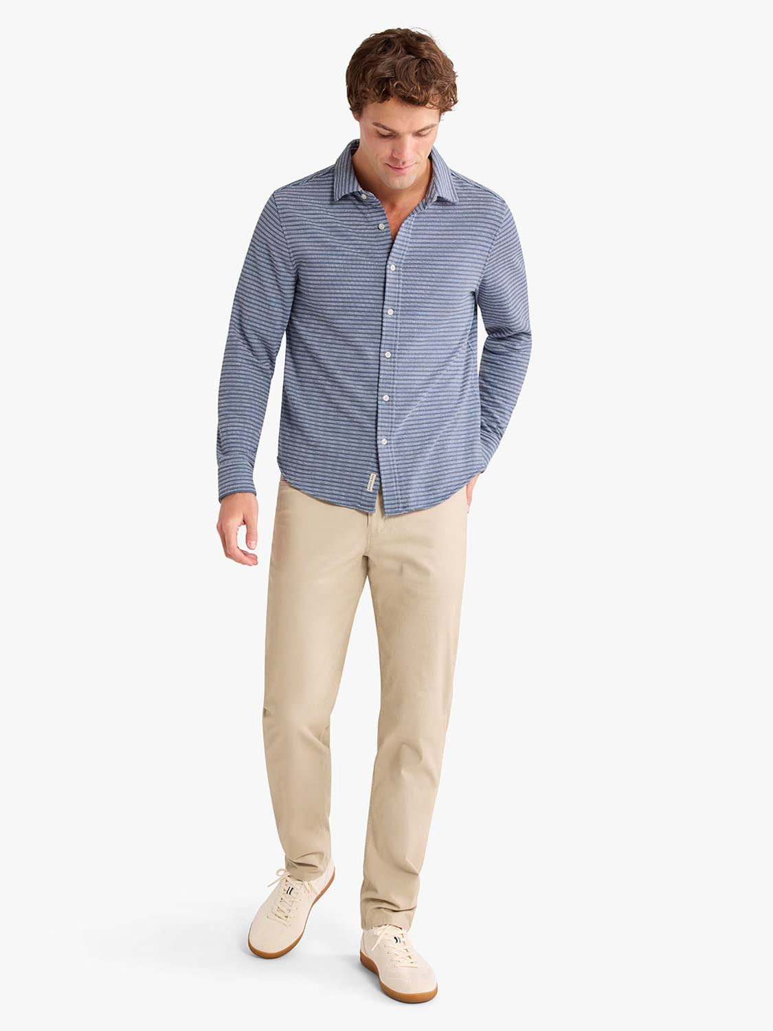 Man wearing a blue striped button-up shirt with khaki pants and cream sneakers.