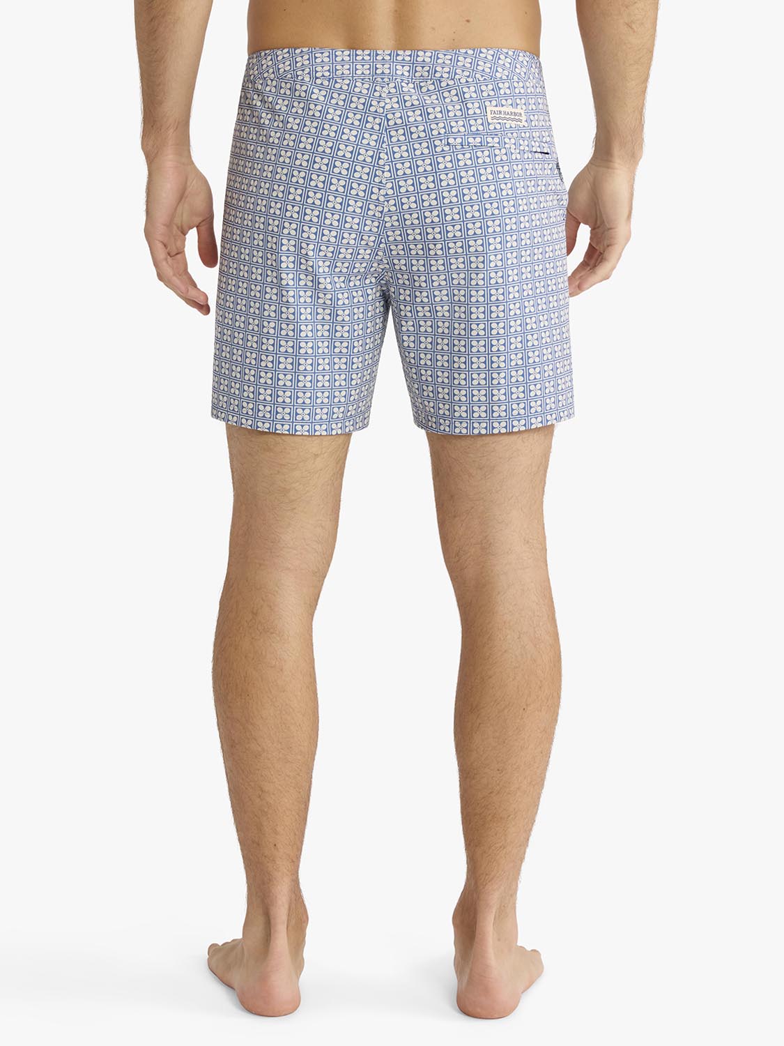 Man wearing blue and white geometric patterned board shorts viewed from behind.