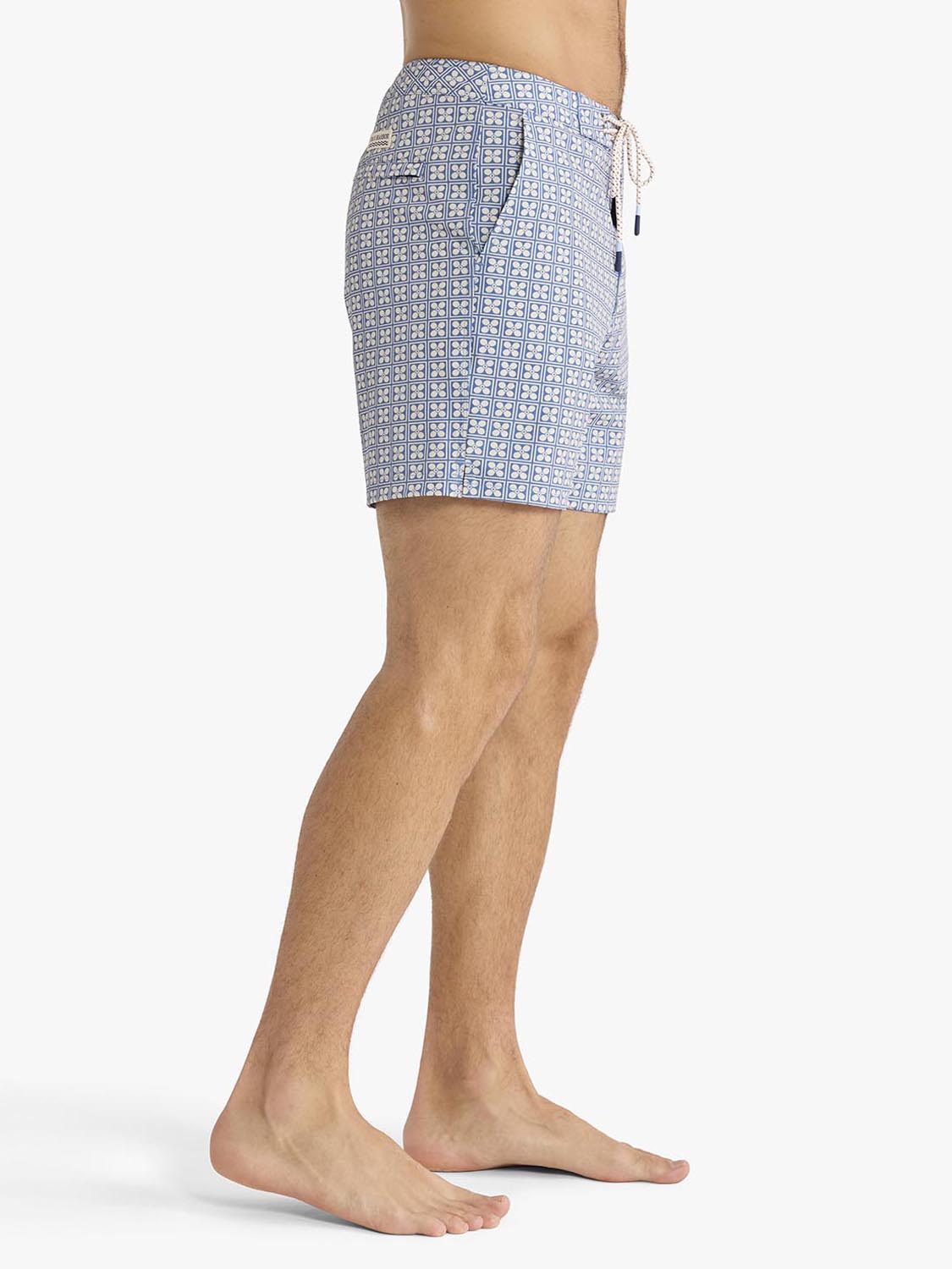 Man wearing blue board shorts with a geometric flower pattern and white drawstring.