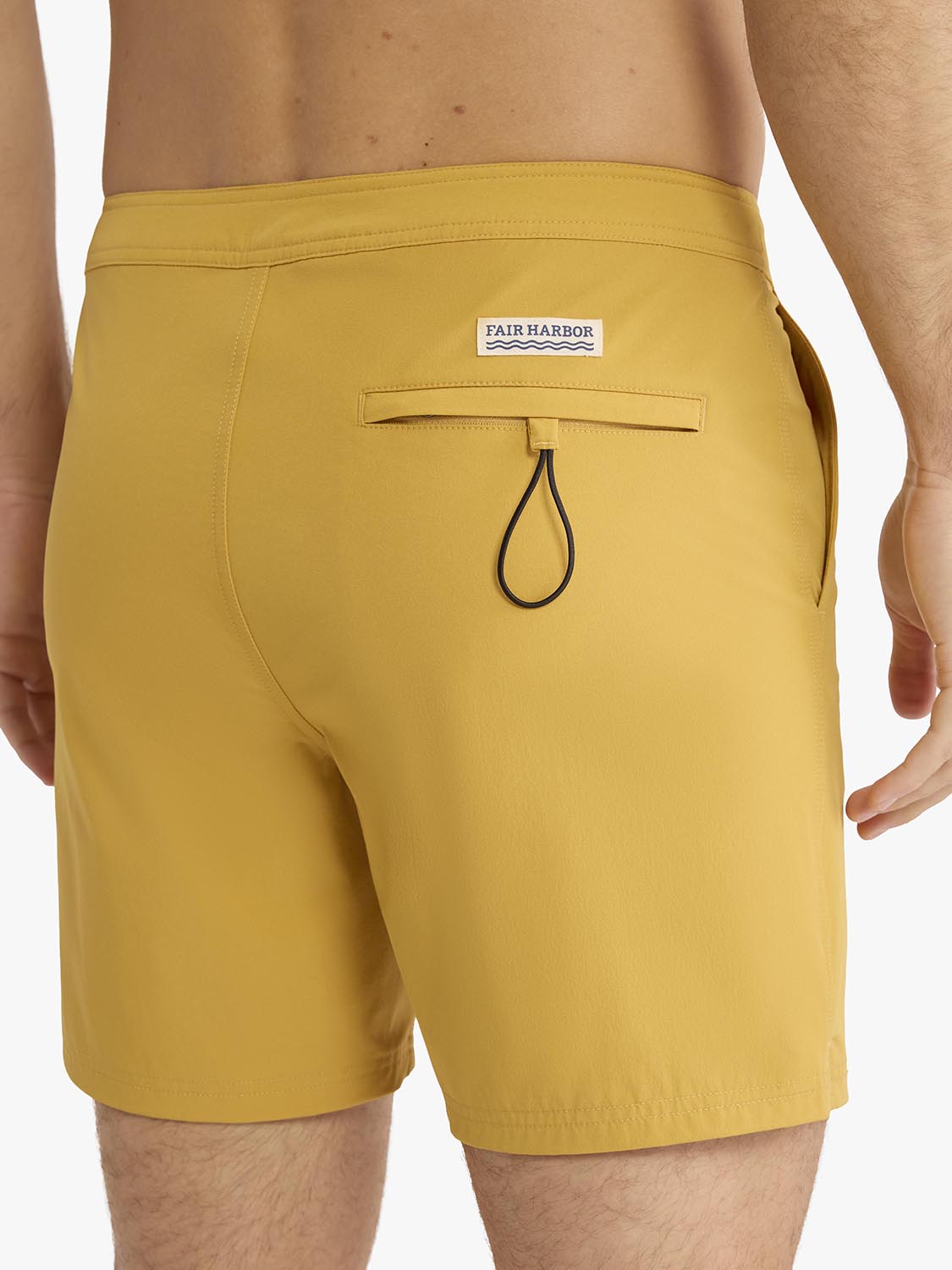Gold board shorts with Fair Harbor branding and a black drawstring closure visible from the back.