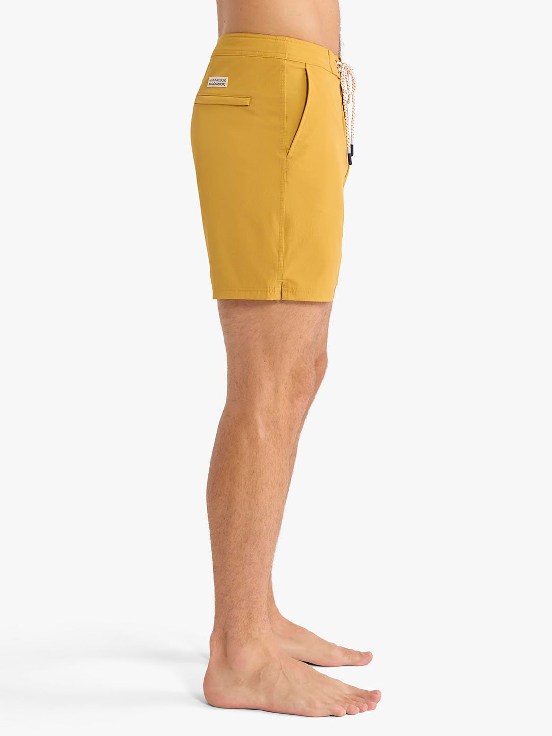 Man wearing gold board shorts with drawstring waistband and back pocket detail.