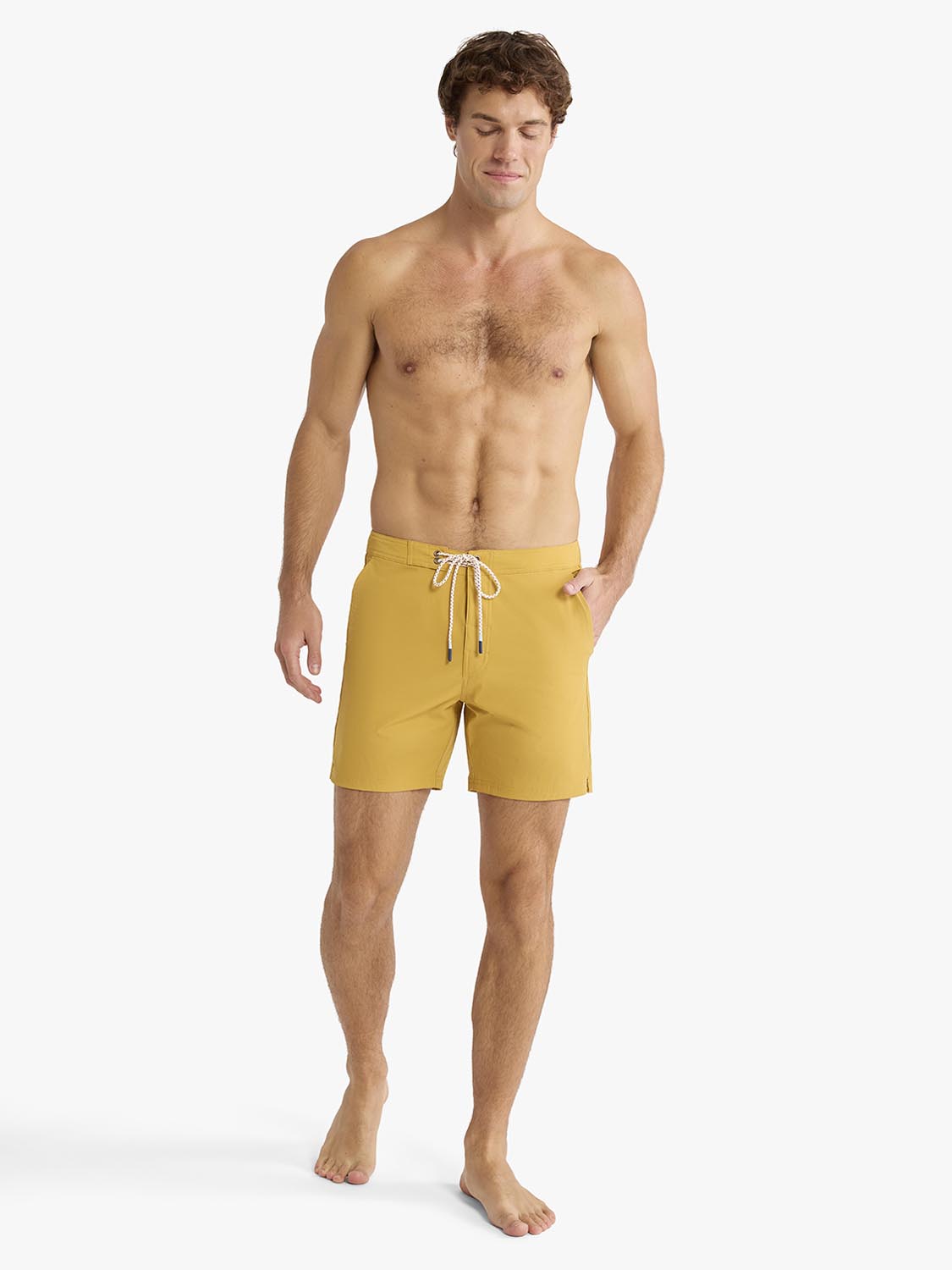 Man wearing gold board shorts with drawstring waist and side pockets against white background.