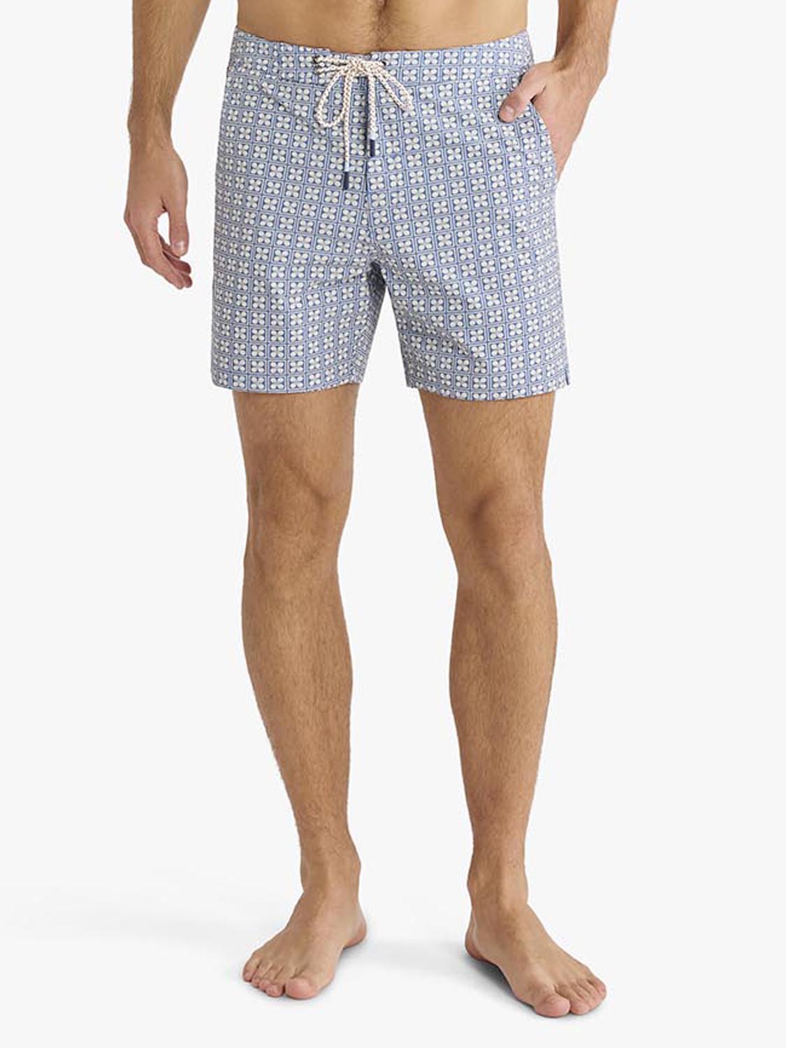 Man wearing blue board shorts with a small geometric flower pattern throughout and a drawstring waist.
