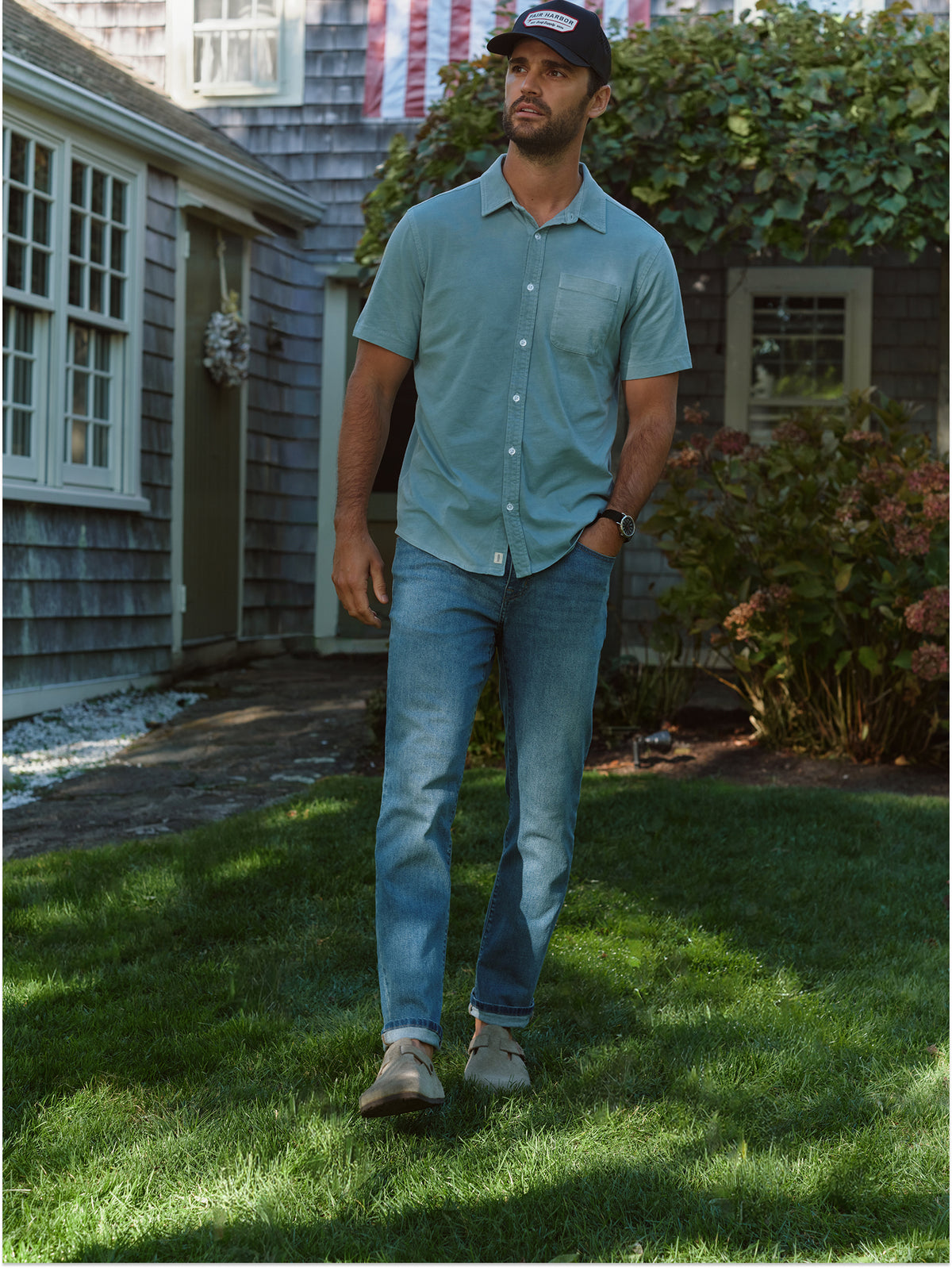 Man wearing a light blue short-sleeve button-up shirt standing in a residential garden setting.