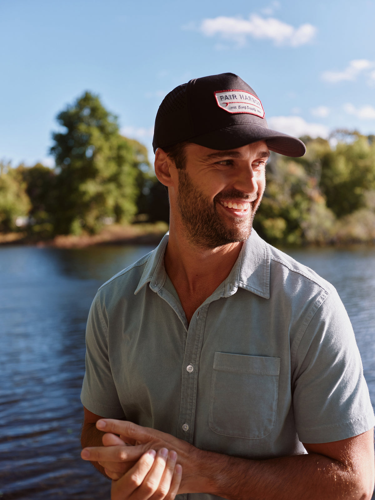 Man wearing a navy short-sleeved button-up shirt standing outdoors by water.