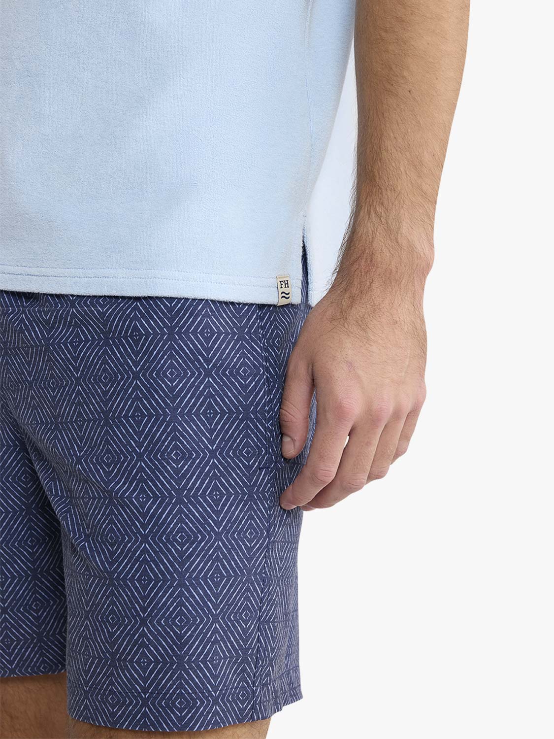 Man wearing light blue terry polo shirt with navy patterned shorts visible at waist.