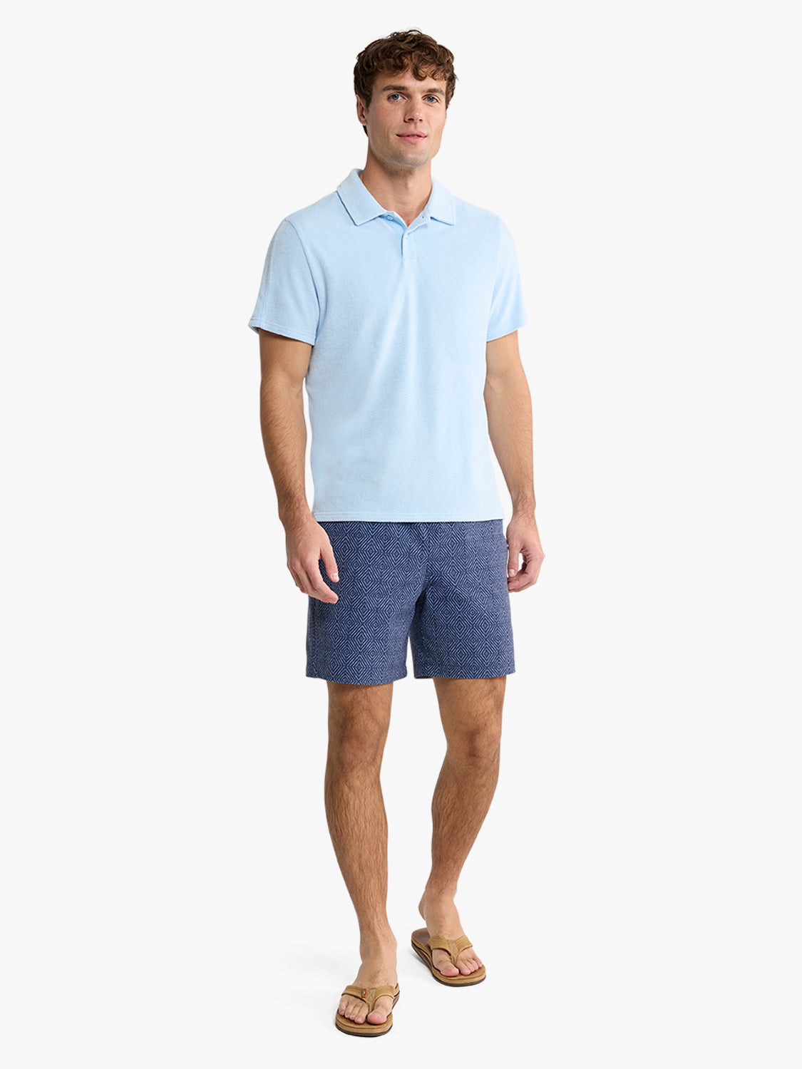 Man wearing a light blue short-sleeve polo shirt with navy blue textured shorts and tan sandals.