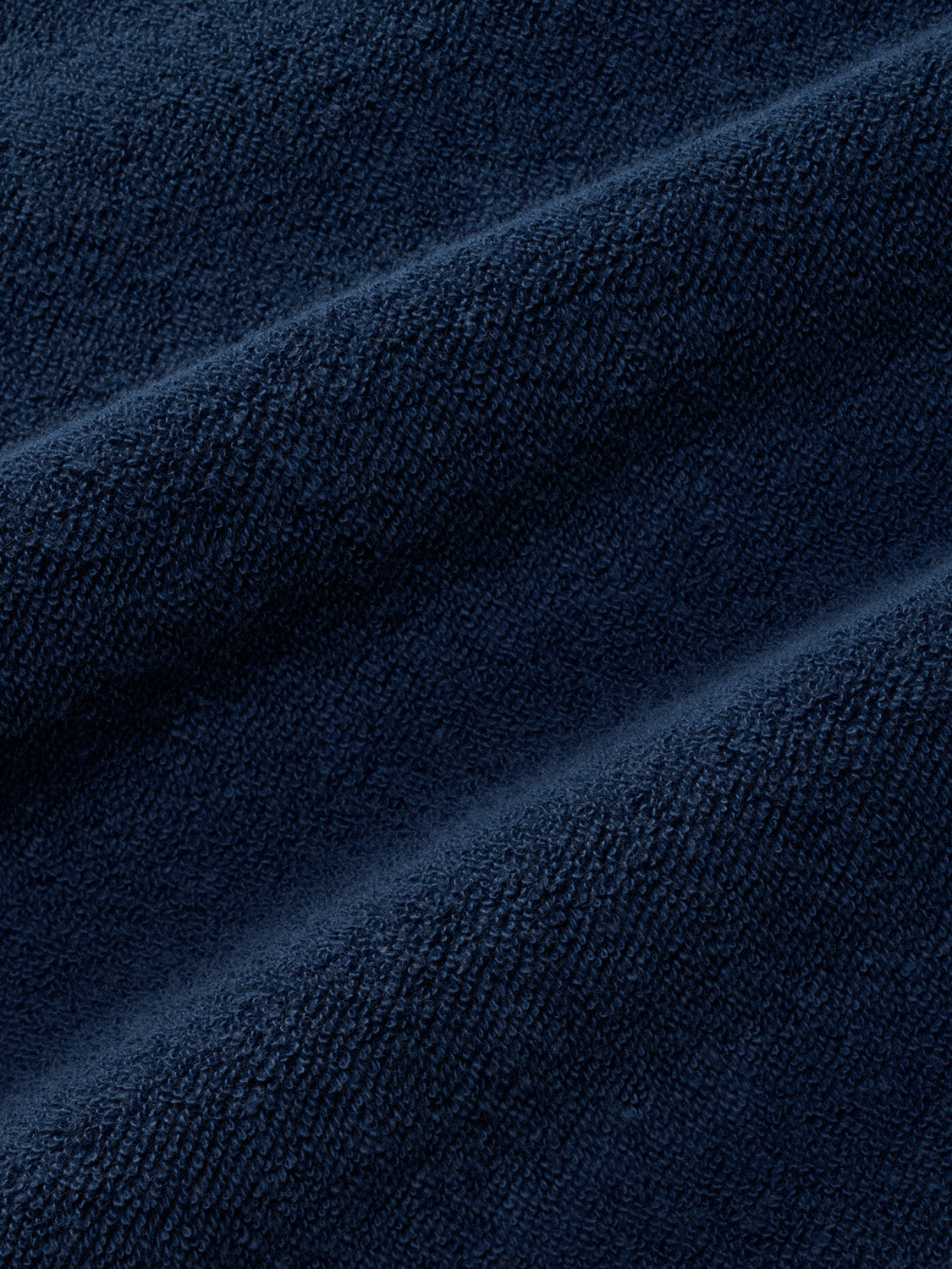 Close-up of navy terry cloth fabric showing textured surface with subtle diagonal folds and draping.