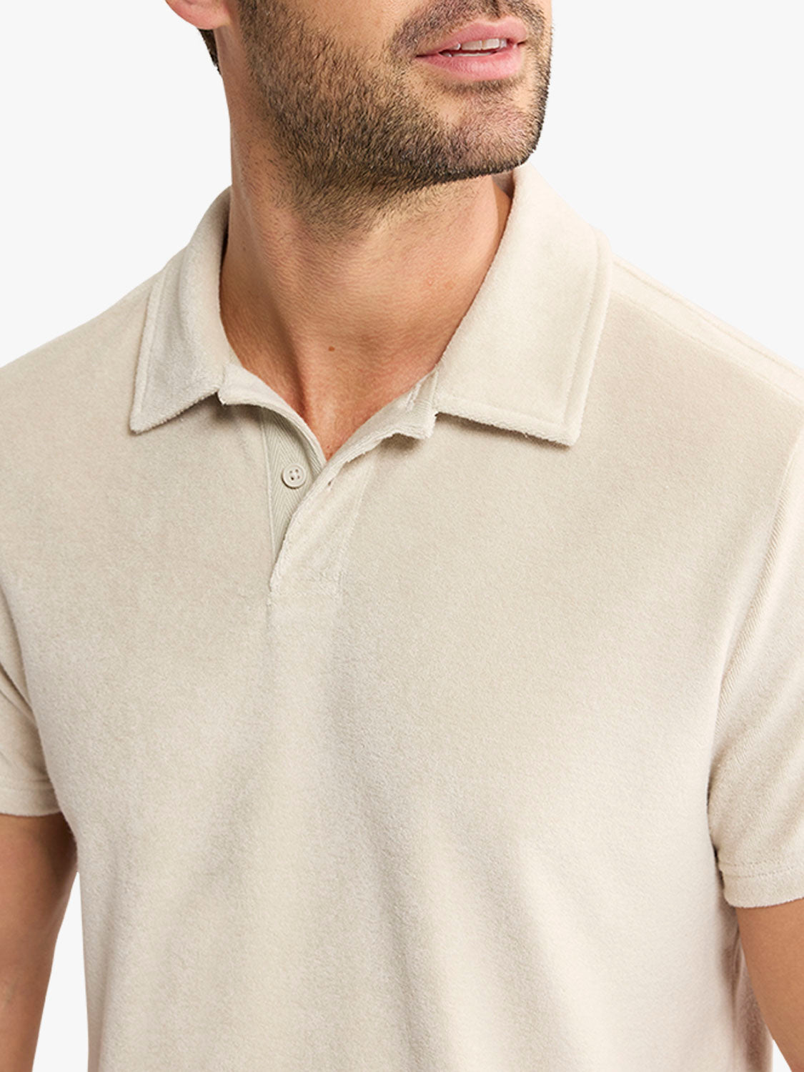 Man wearing a sand-colored terry polo shirt with a collared neckline and button placket.
