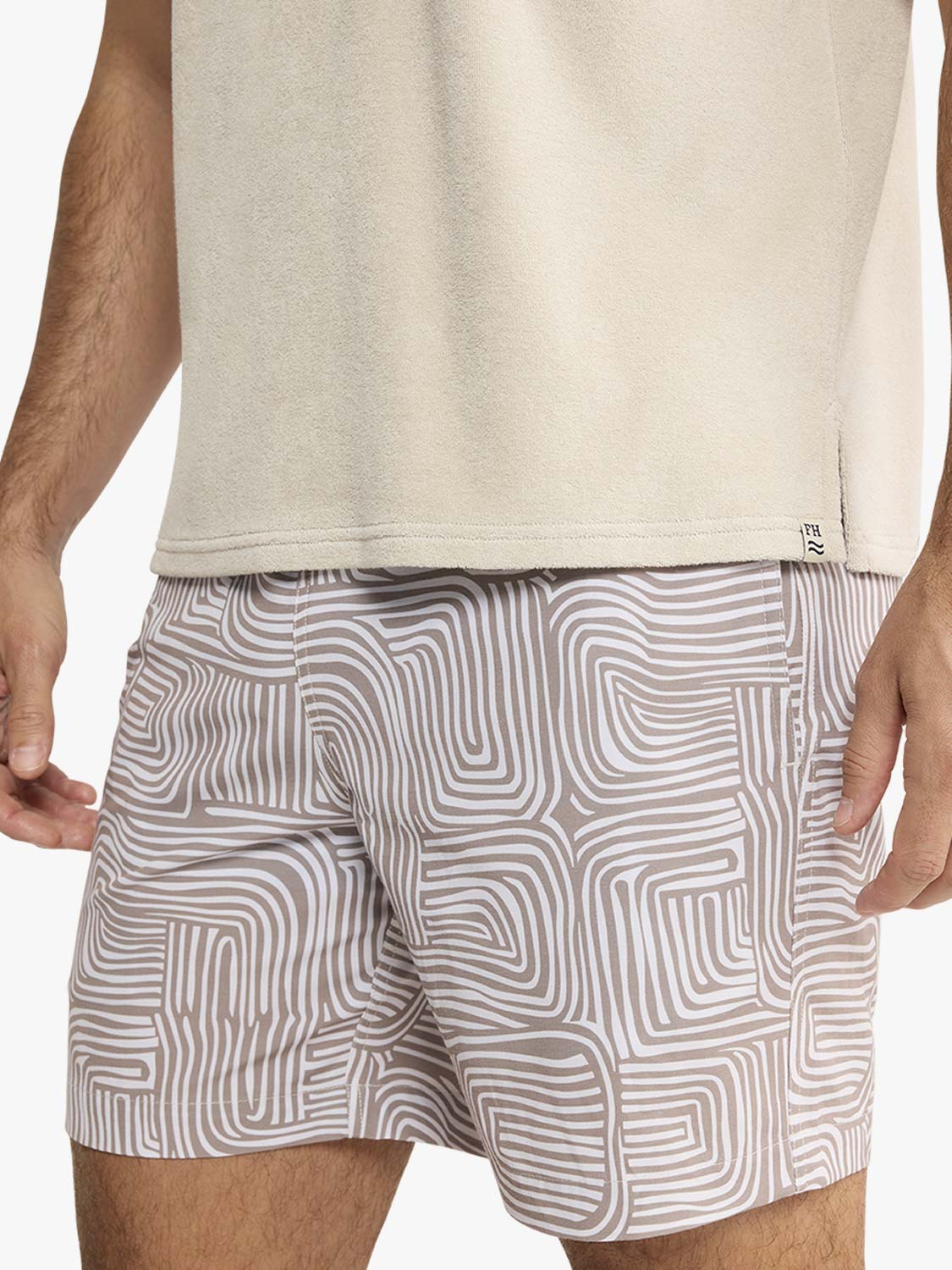 Man wearing a sand-colored terry polo shirt with patterned shorts featuring curved geometric stripes.