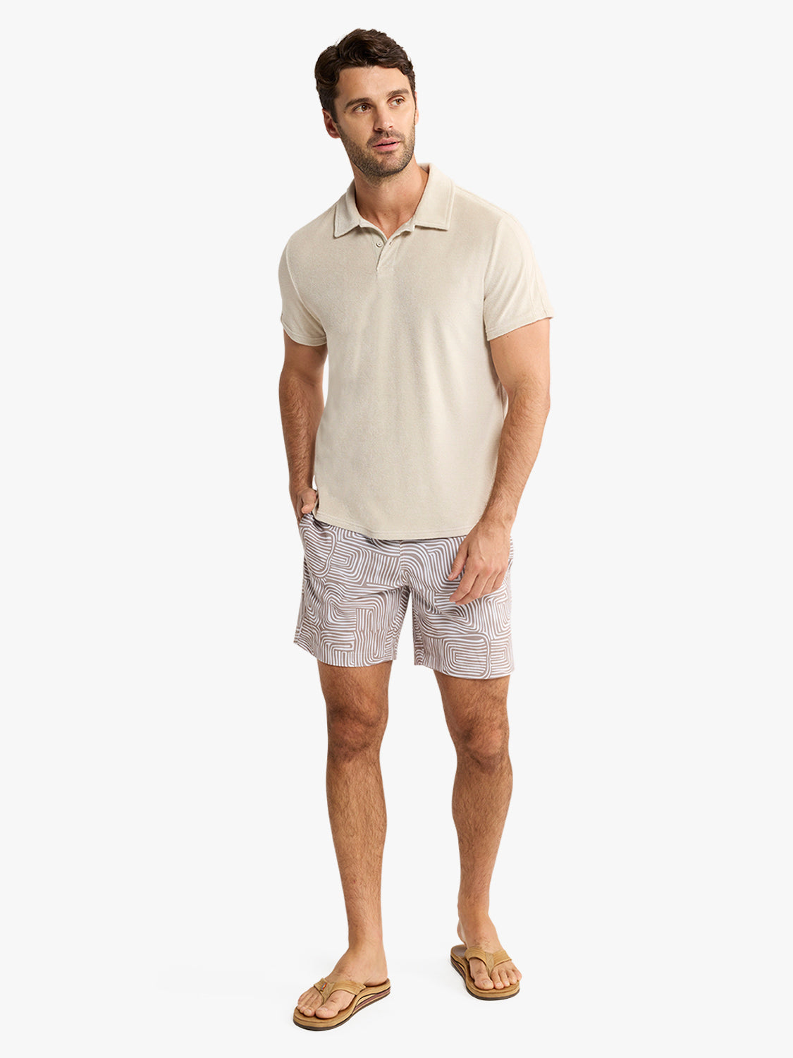 Man wearing sand-colored terry polo shirt with geometric patterned shorts and sandals.