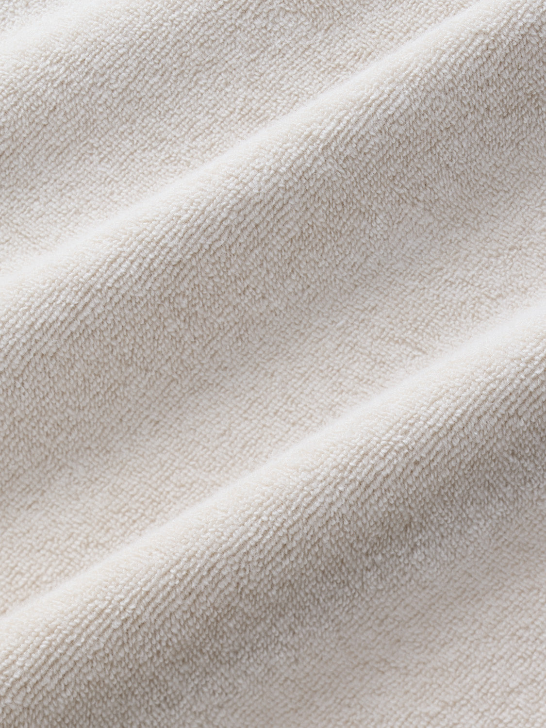 Close-up of sand-colored terry fabric with diagonal ribbed texture and soft draping folds.