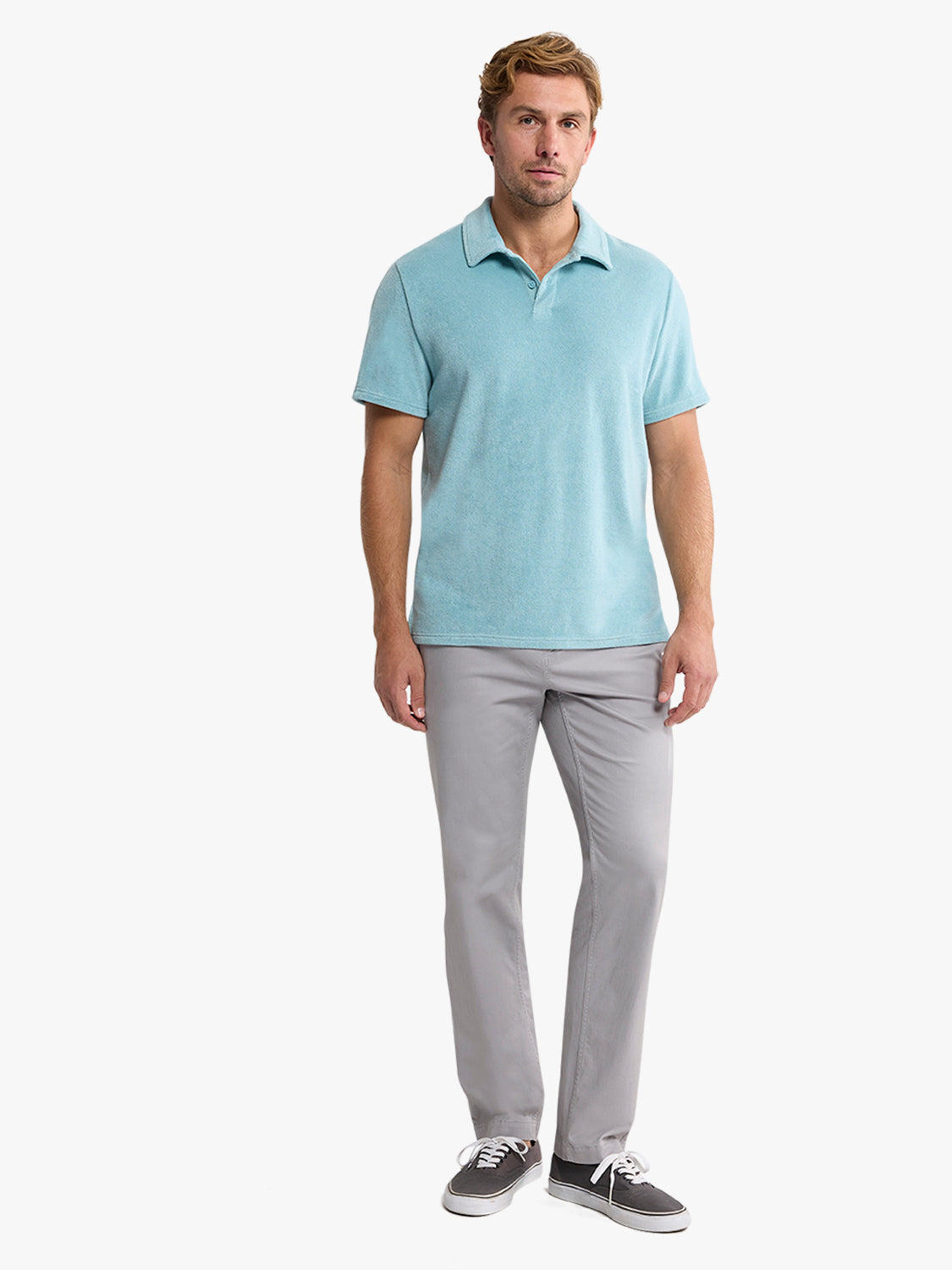 Man wearing a light blue short-sleeve polo shirt with gray pants and dark sneakers.