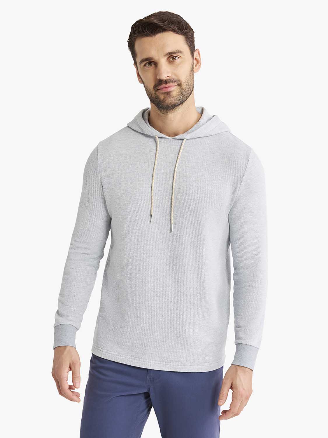 Man wearing a heather grey hoodie with drawstring and long sleeves over navy pants.