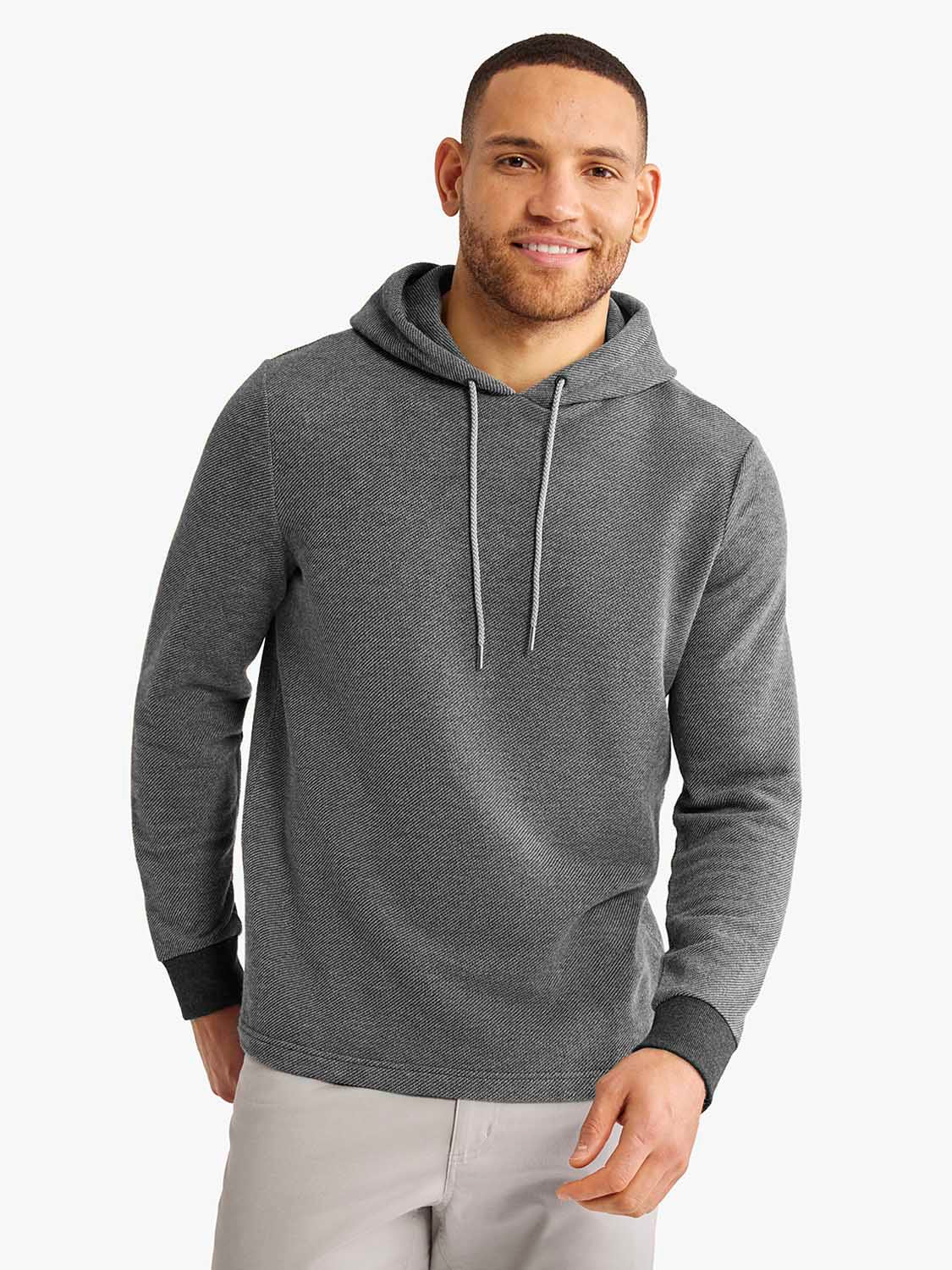 Man wearing a charcoal gray hoodie with drawstring and black ribbed cuffs over light gray pants.